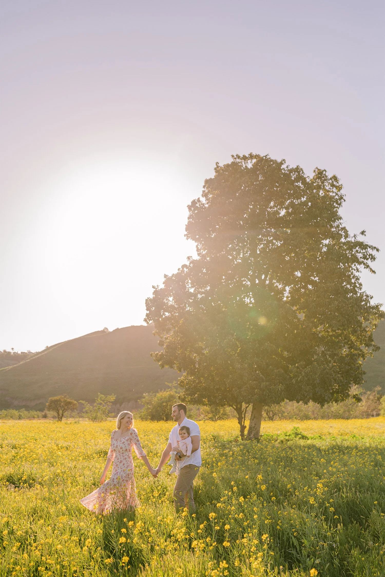 Orange County family photographer photographs parents holding hands with their daughter in a golden mustard field