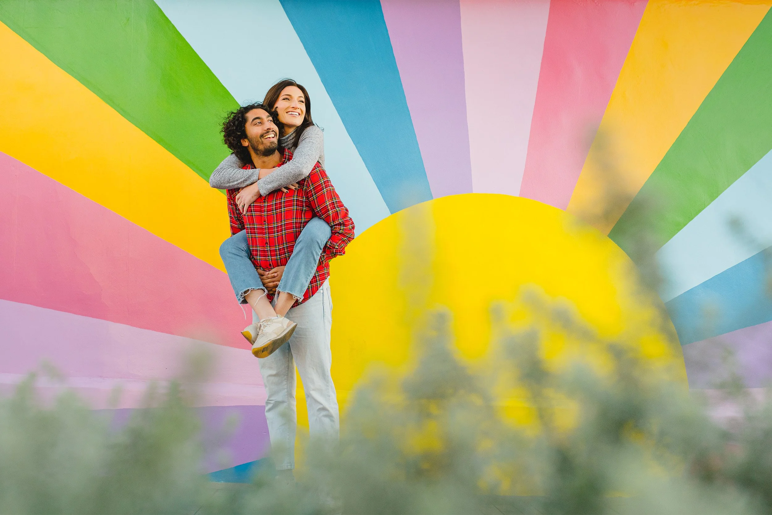 Award-winning engagement photographer captures couple laughing together against a playful sunburst mural in Manhattan Beach