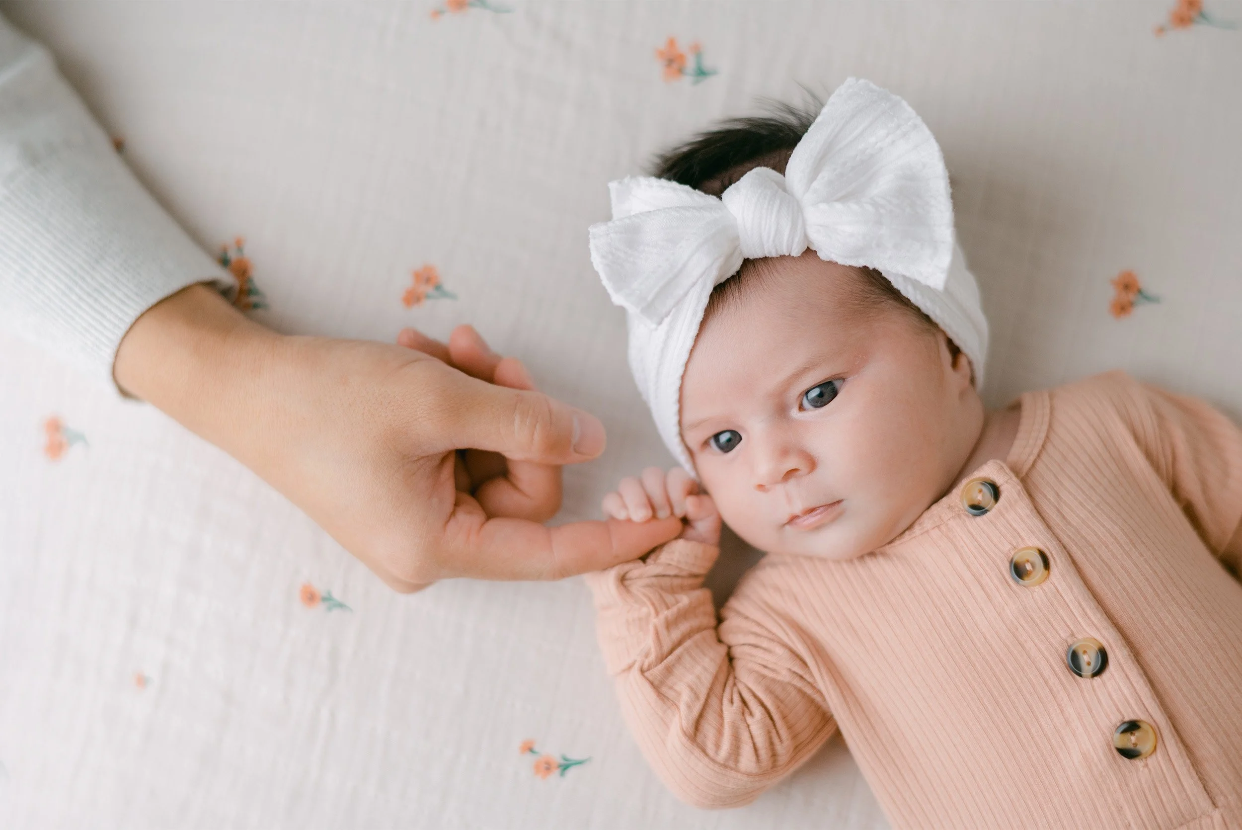 Newborn in peach outfit holding mother's finger, close-up portrait, award-winning baby photographer in Orange County