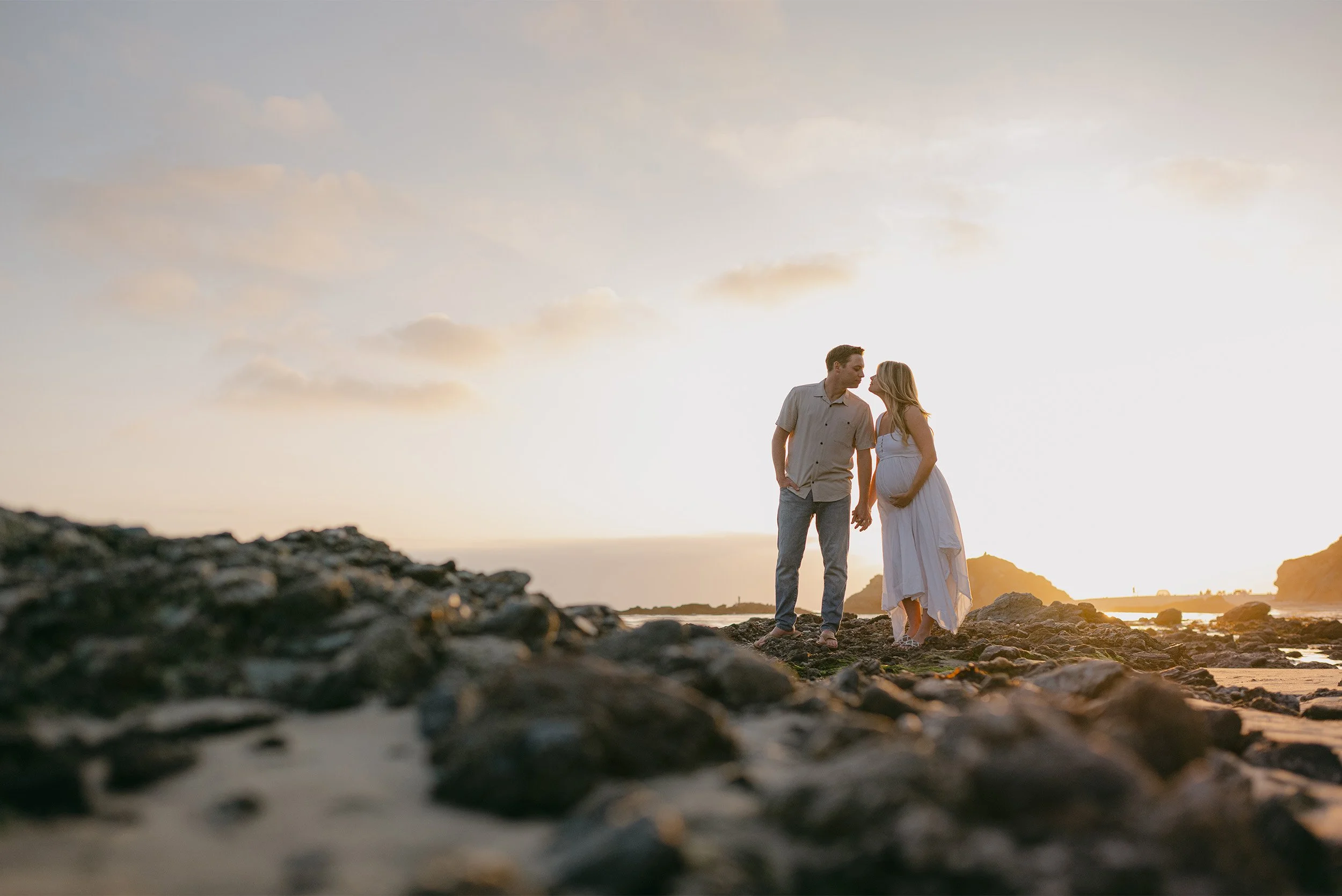 Couple standing close on rocky beach in Laguna Beach at golden hour, highly recommended maternity photographer in Laguna Beach