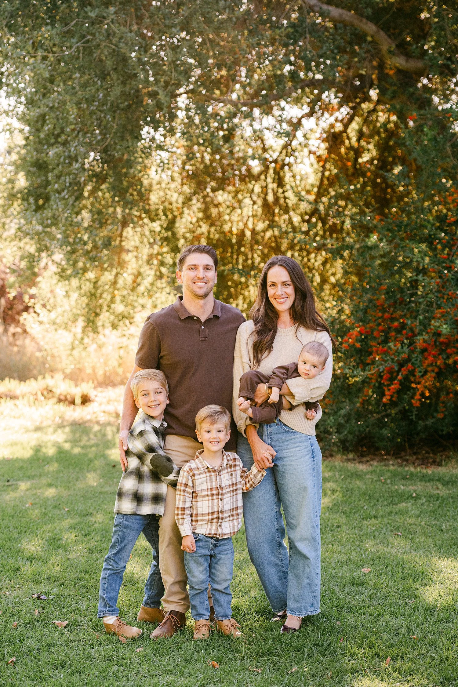 Orange County family photographer captures family of five smiling together under a golden tree at sunset