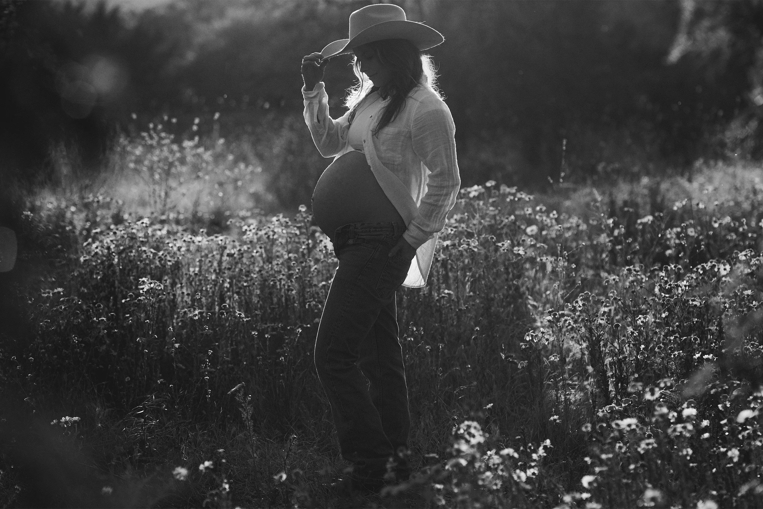 Black and white silhouette of pregnant woman in cowboy hat in wildflower field, Orange County maternity photographer