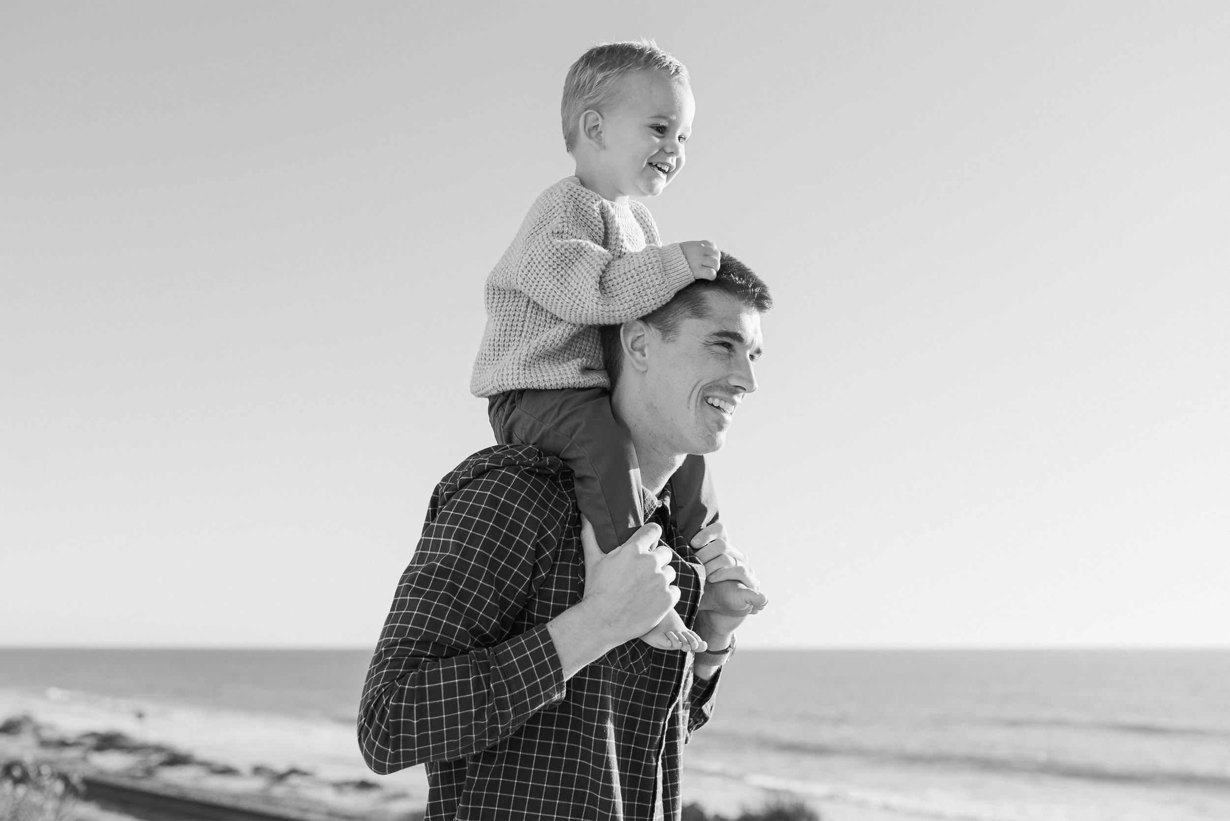 Award-winning family photographer in Orange County captures black-and-white portrait of toddler on father's shoulders at beach