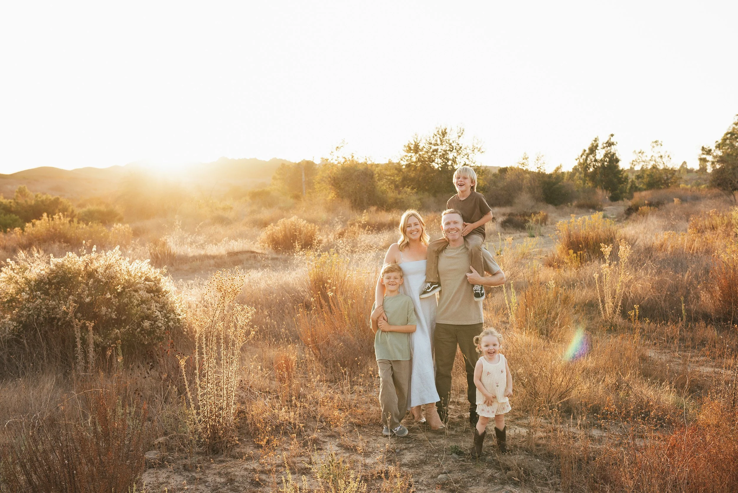 Award-winning family photographer in Orange County photographs family portrait in sunlit meadow in Irvine Park