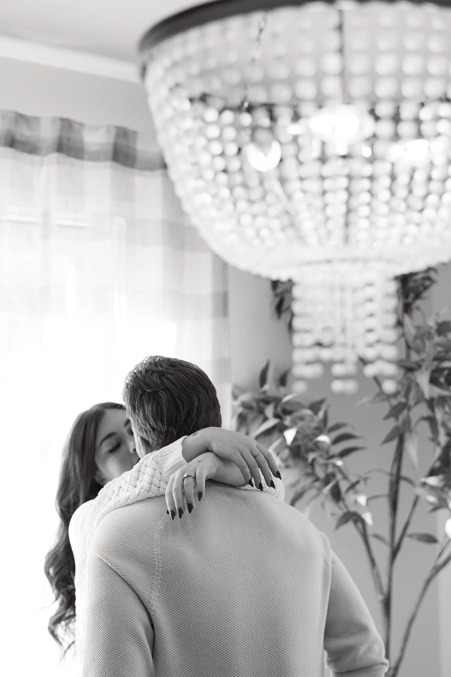 Award-winning engagement photographer in Orange County captures intimate embrace beneath crystal chandelier in black and white at a home engagement session