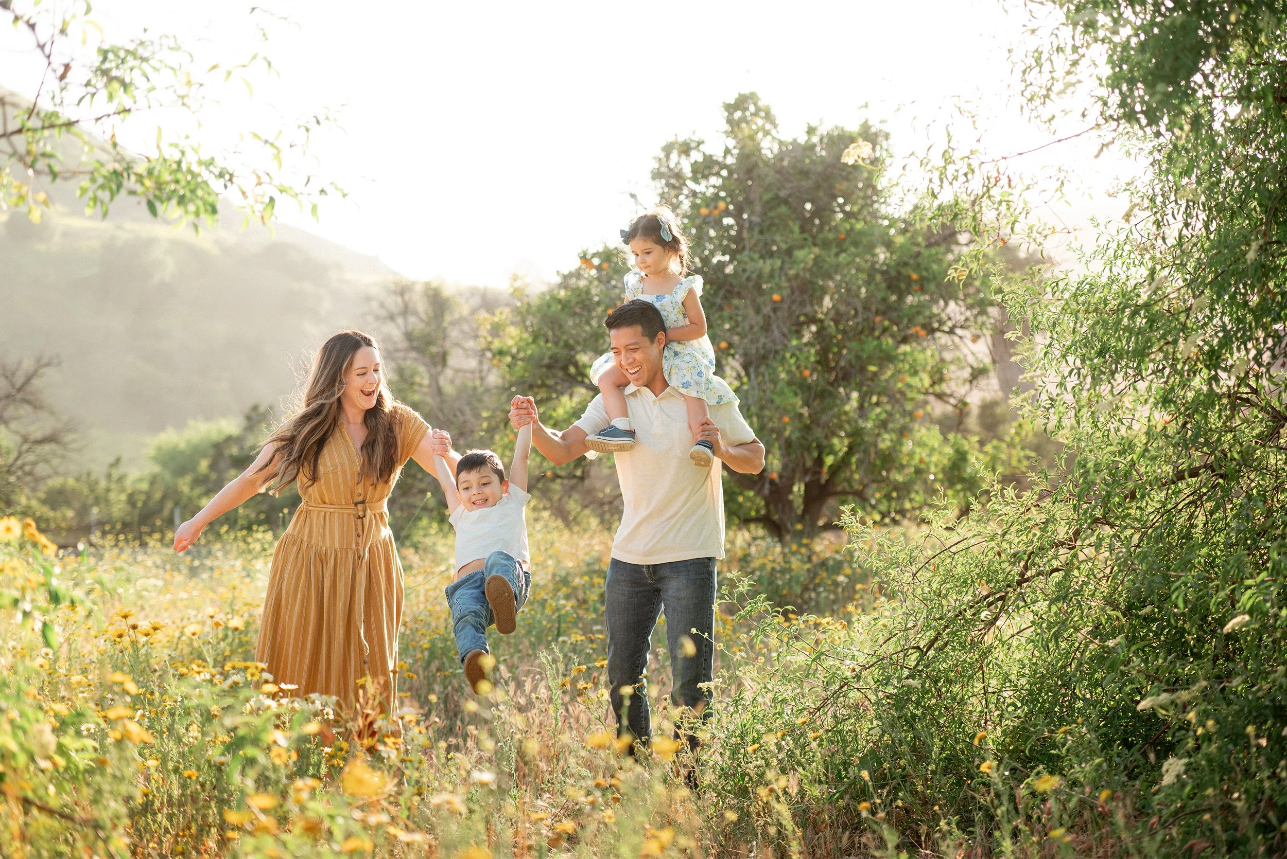 Orange County family photographer captures family of four walking through wildflower field at golden hour