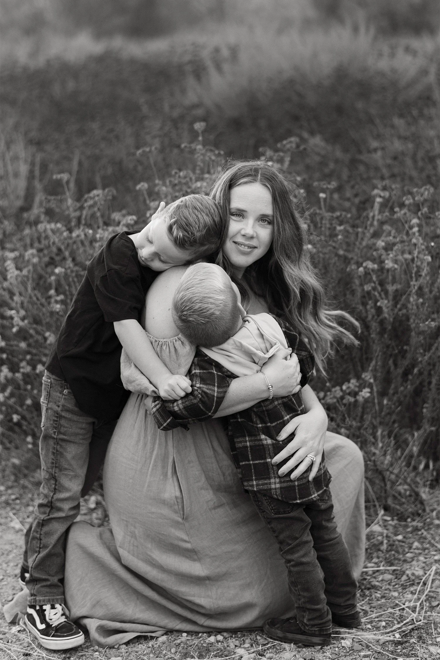Award-winning family photographer captures mother hugging her two sons closely in a wildflower field in Orange County