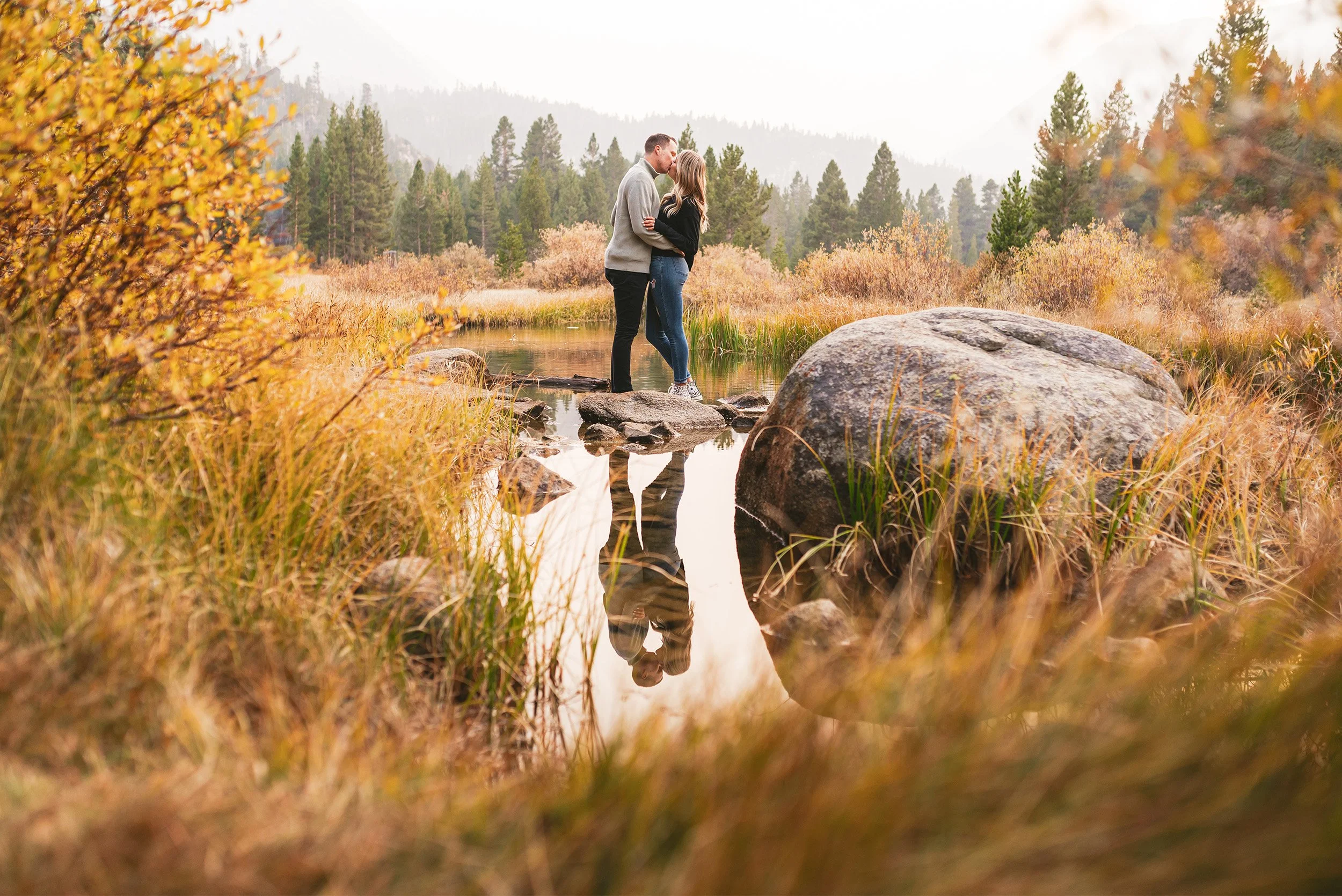 Engaged couple kissing by a mountain lake reflection during golden hour engagement session in the Eastern Sierras