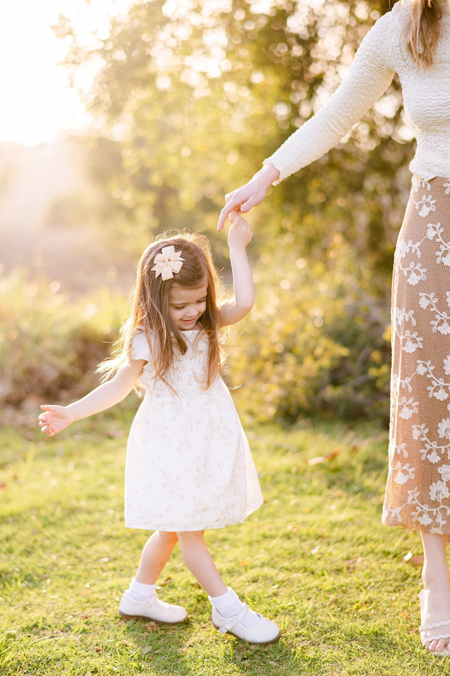 Family photography session in Orange County featuring little girl twirling while holding her mother's hand in golden light