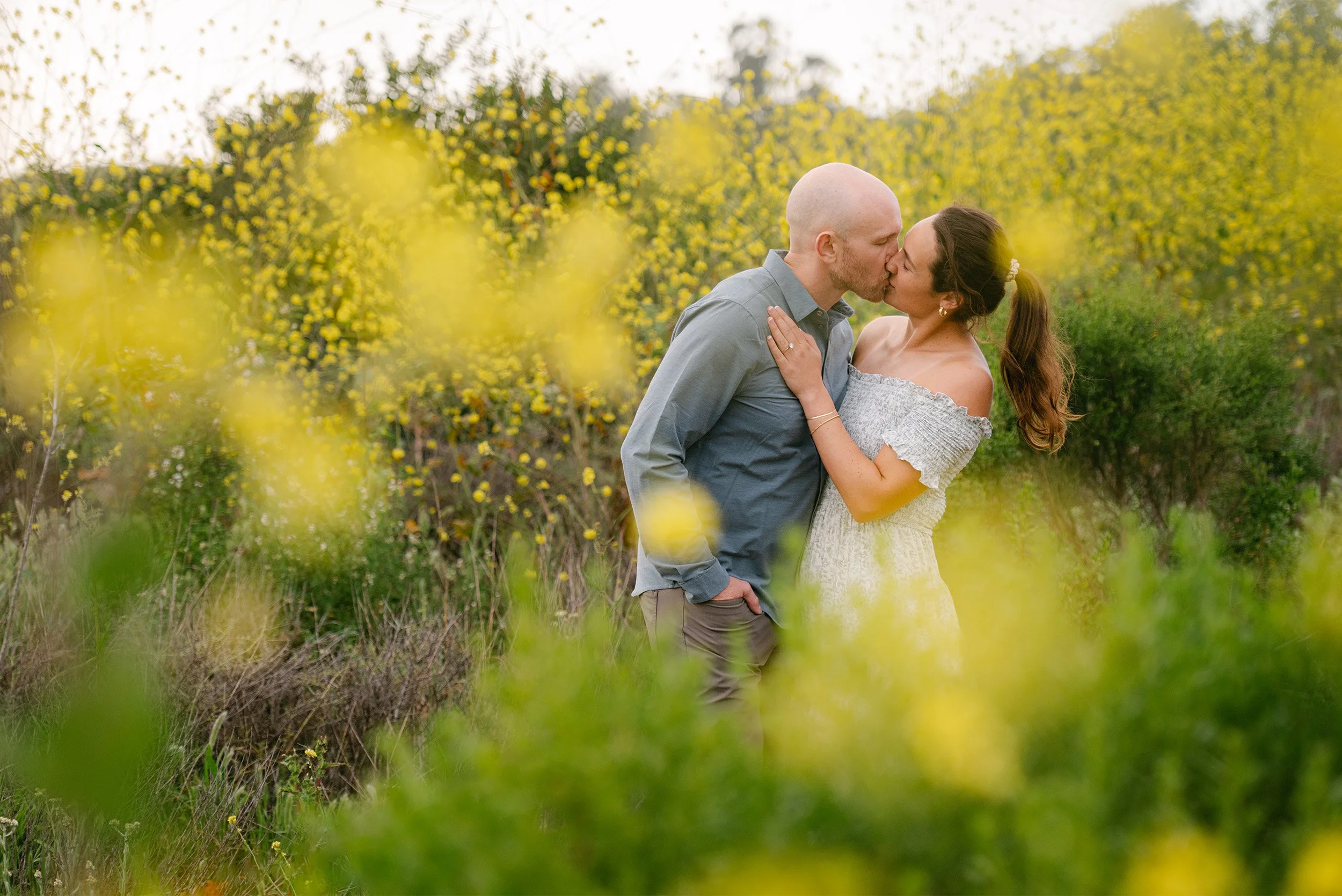 Award-winning engagement photographer in Orange County captures couple kissing amid blooming yellow wildflowers at Crystal Cove