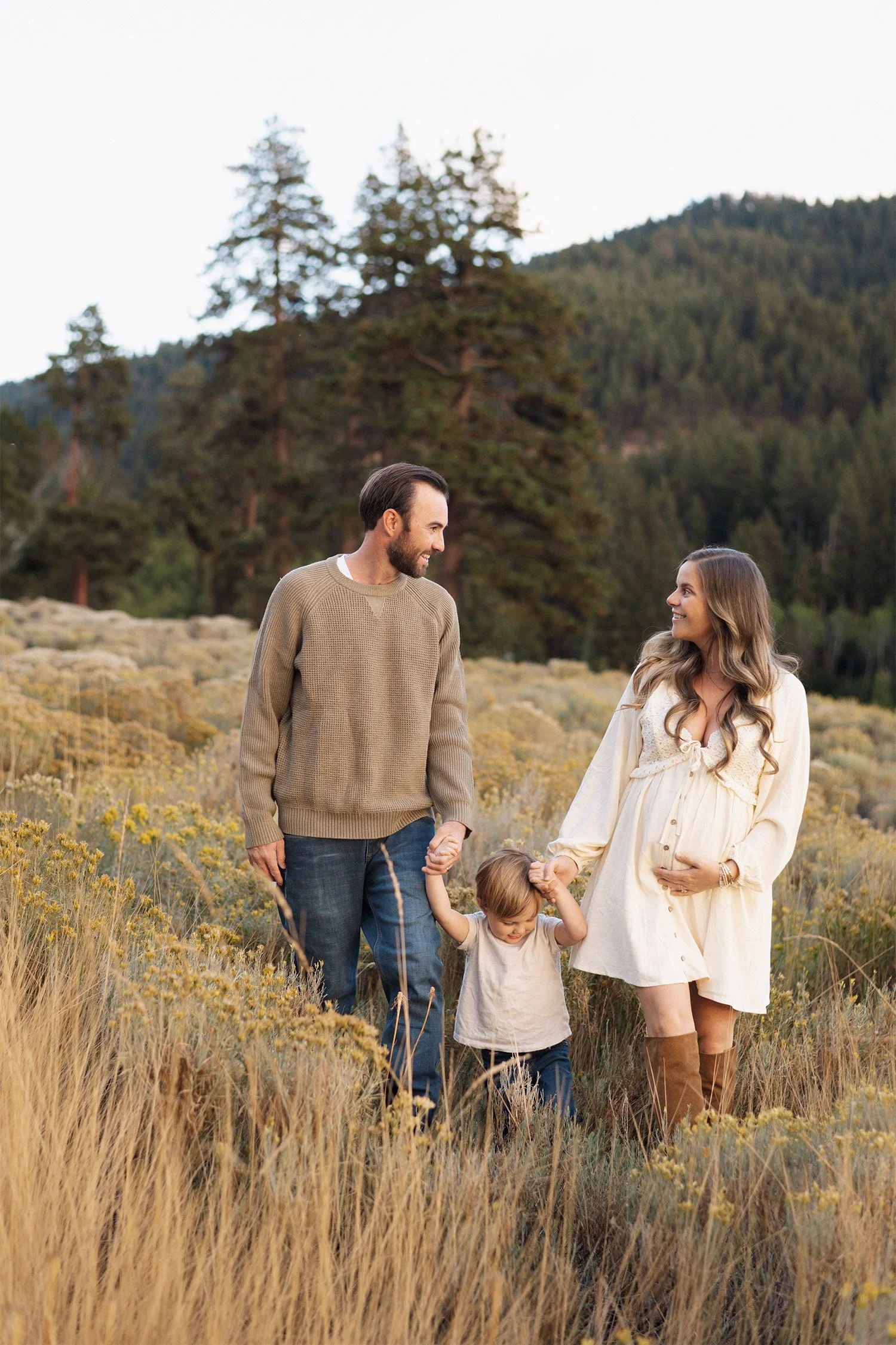 Pregnant mother and father walking with toddler through a mountain meadow, Highly recommended family photographer in Orange County