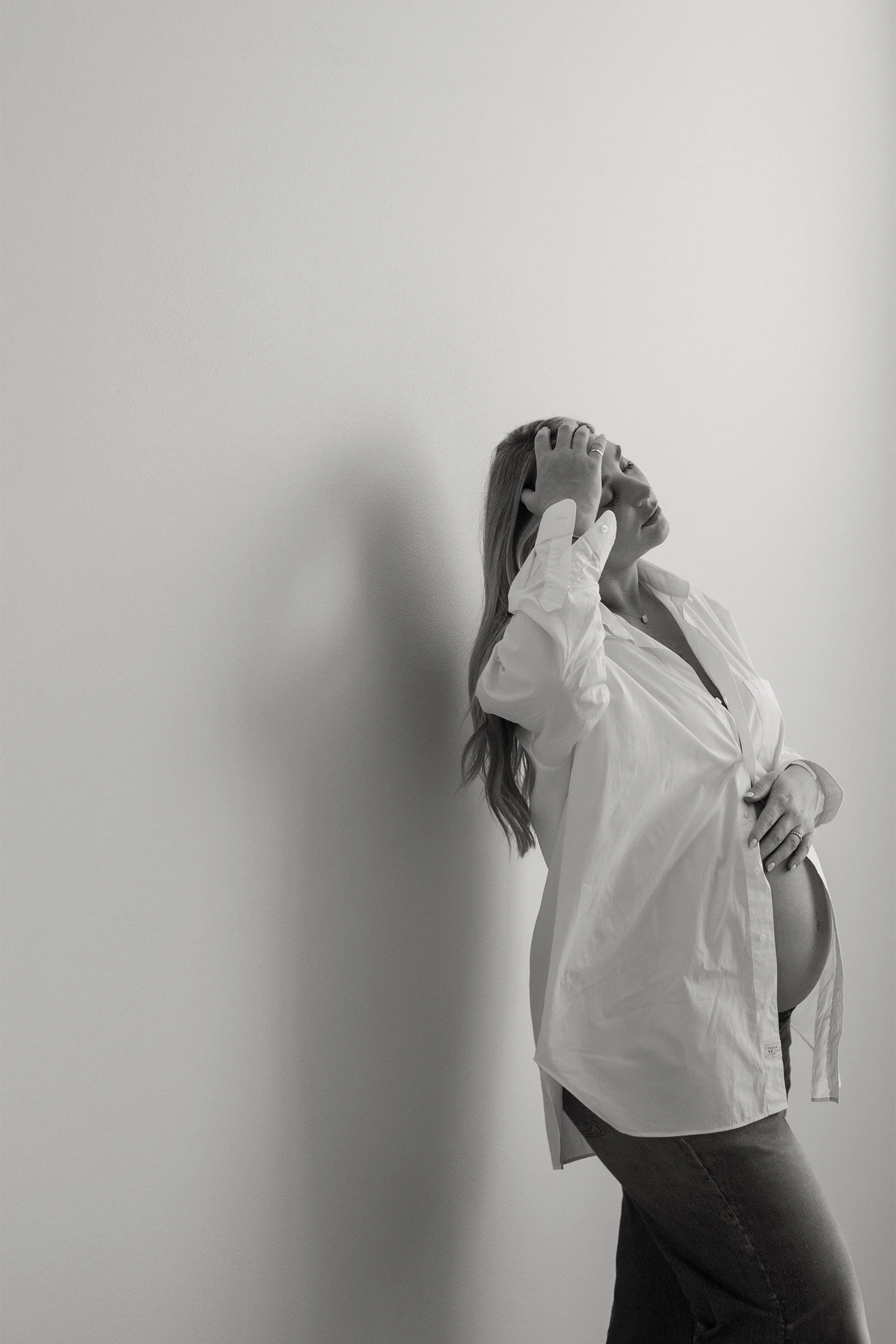 Black and white profile of pregnant woman in a white button down leaning against wall, award-winning maternity photographer in Orange County