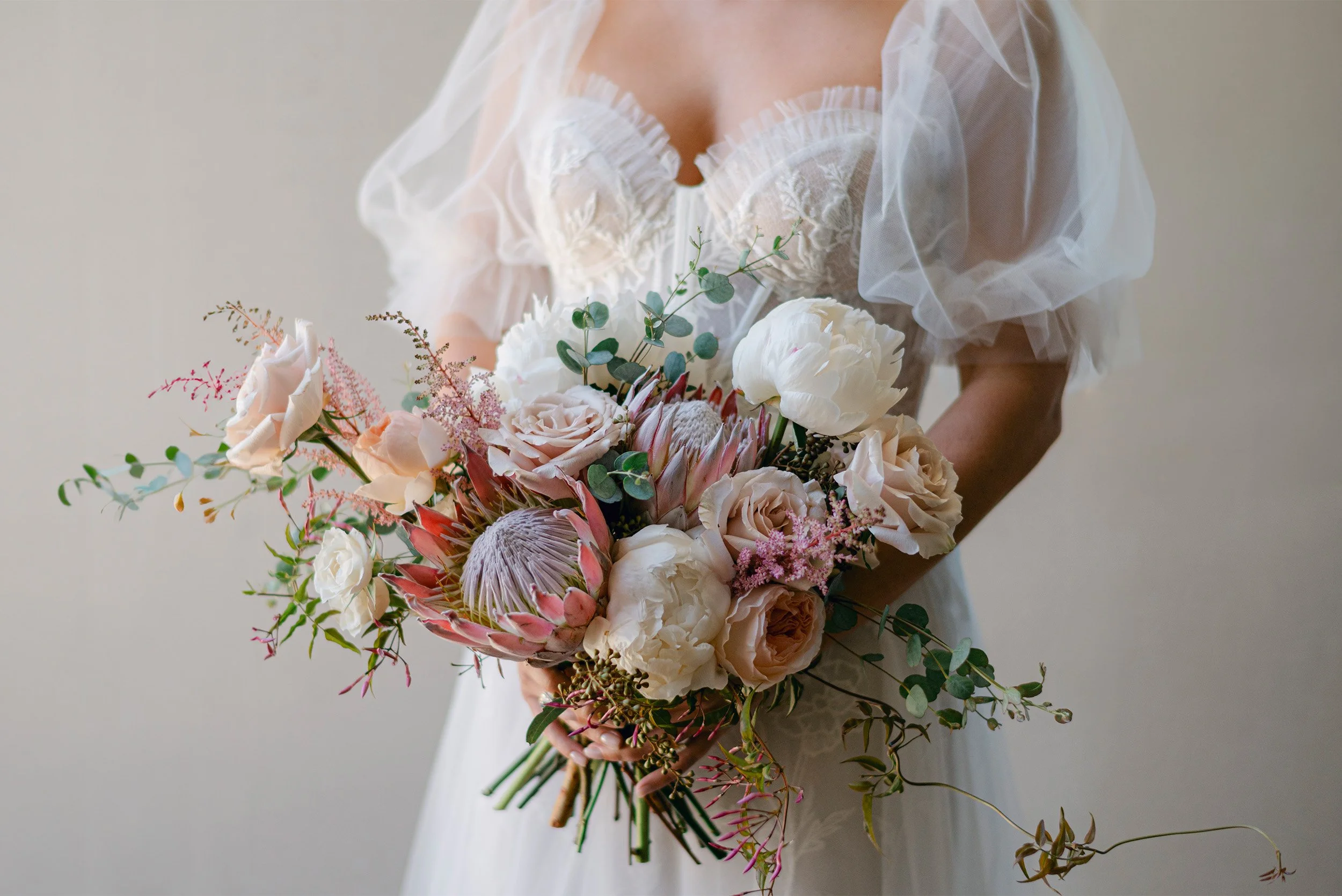 Bride holding lush bouquet of peonies, roses, and king protea flowers, close-up bridal detail photo