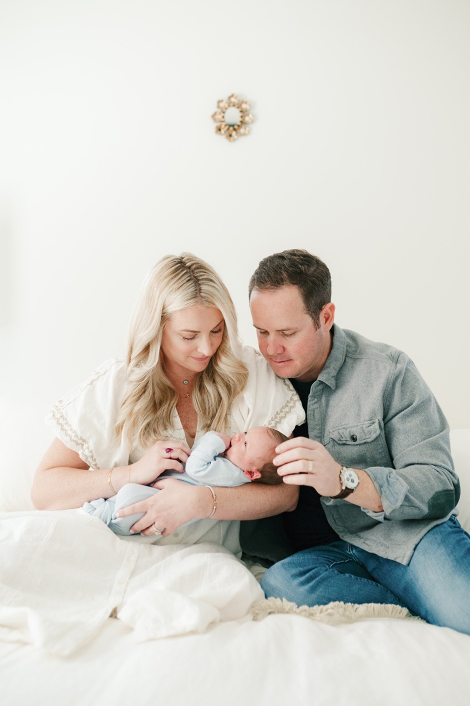 Orange County newborn photographer captures parents gazing tenderly at sleeping baby boy on bed in bright, airy nursery, in home newborn baby photos