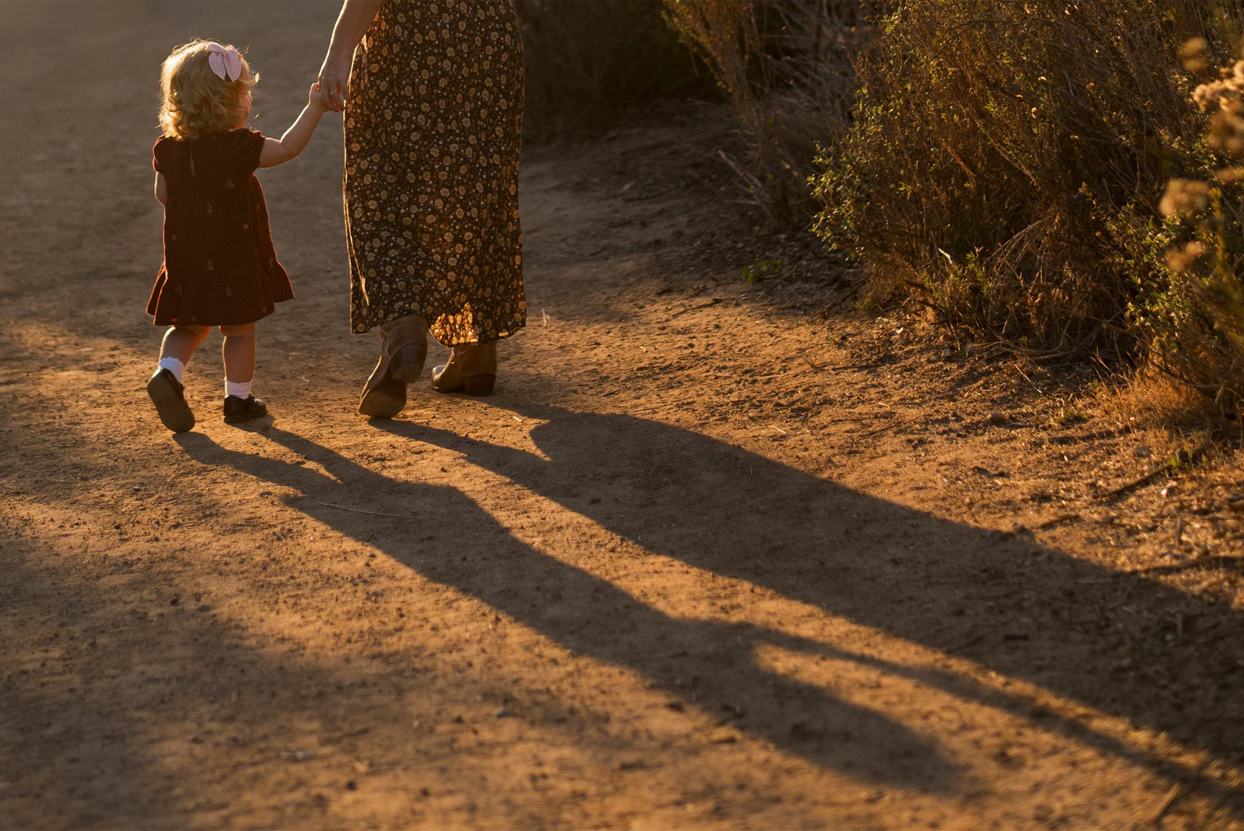 Toddler holding mother's hand on sunlit dirt path, Award-winning family photographer in Orange County