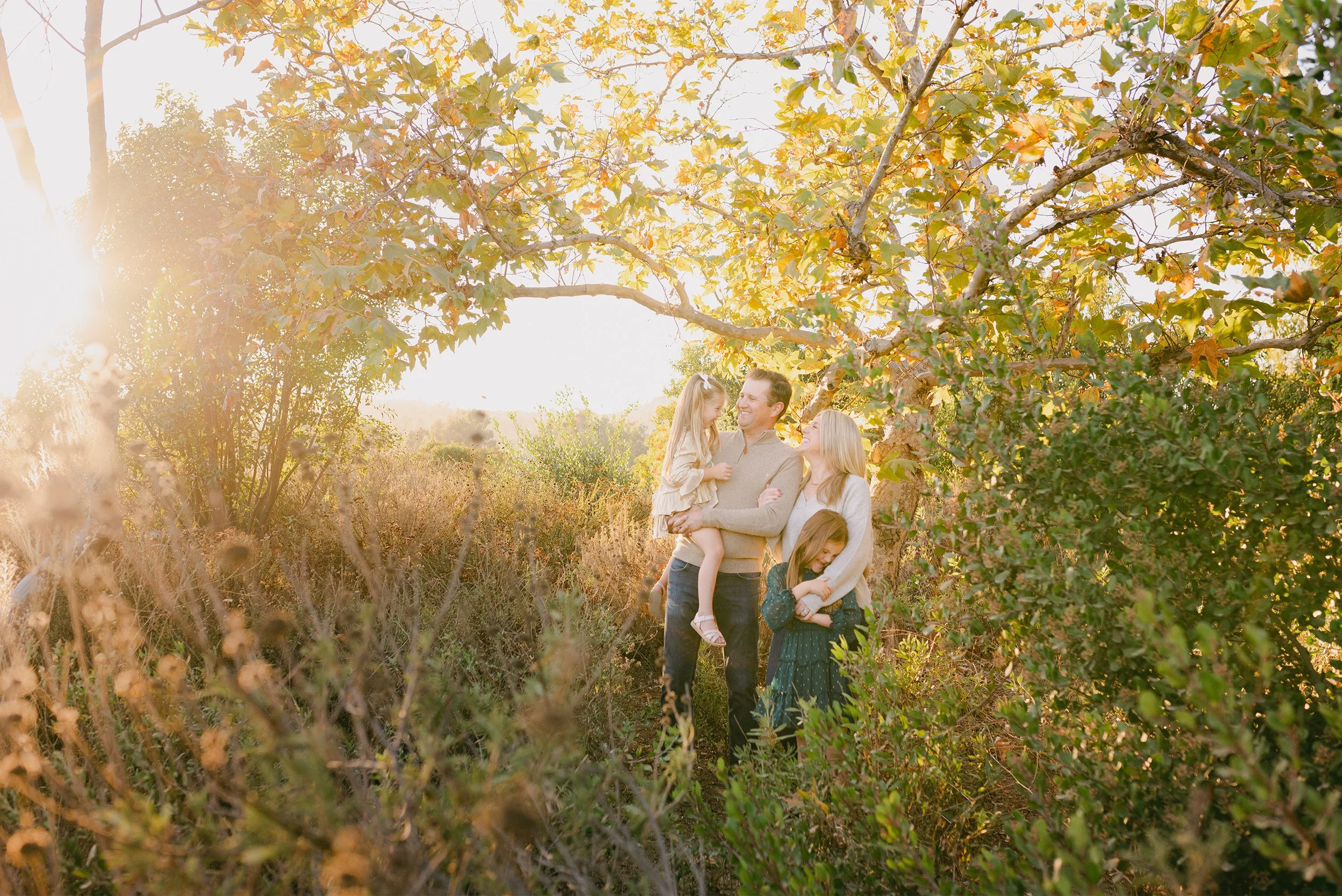 Family portrait photography in Orange County featuring family laughing beneath golden autumn tree canopy