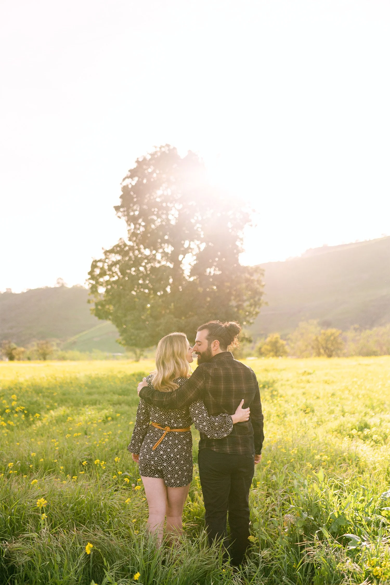 Highly recommended engagement photographer in Orange County captures couple embracing in golden wildflower field at sunset