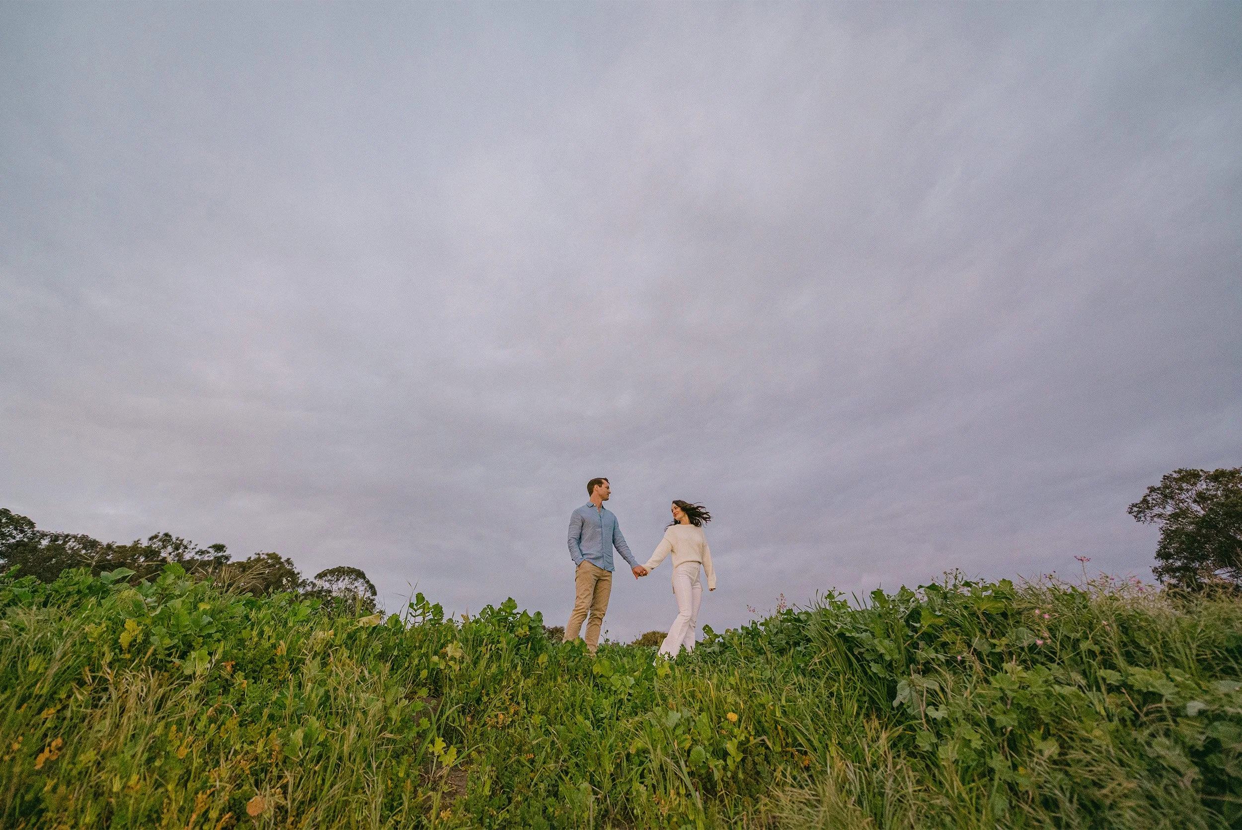 Highly recommended Santa Barbara engagement photographer captures couple holding hands beneath a dramatic cloudy sky