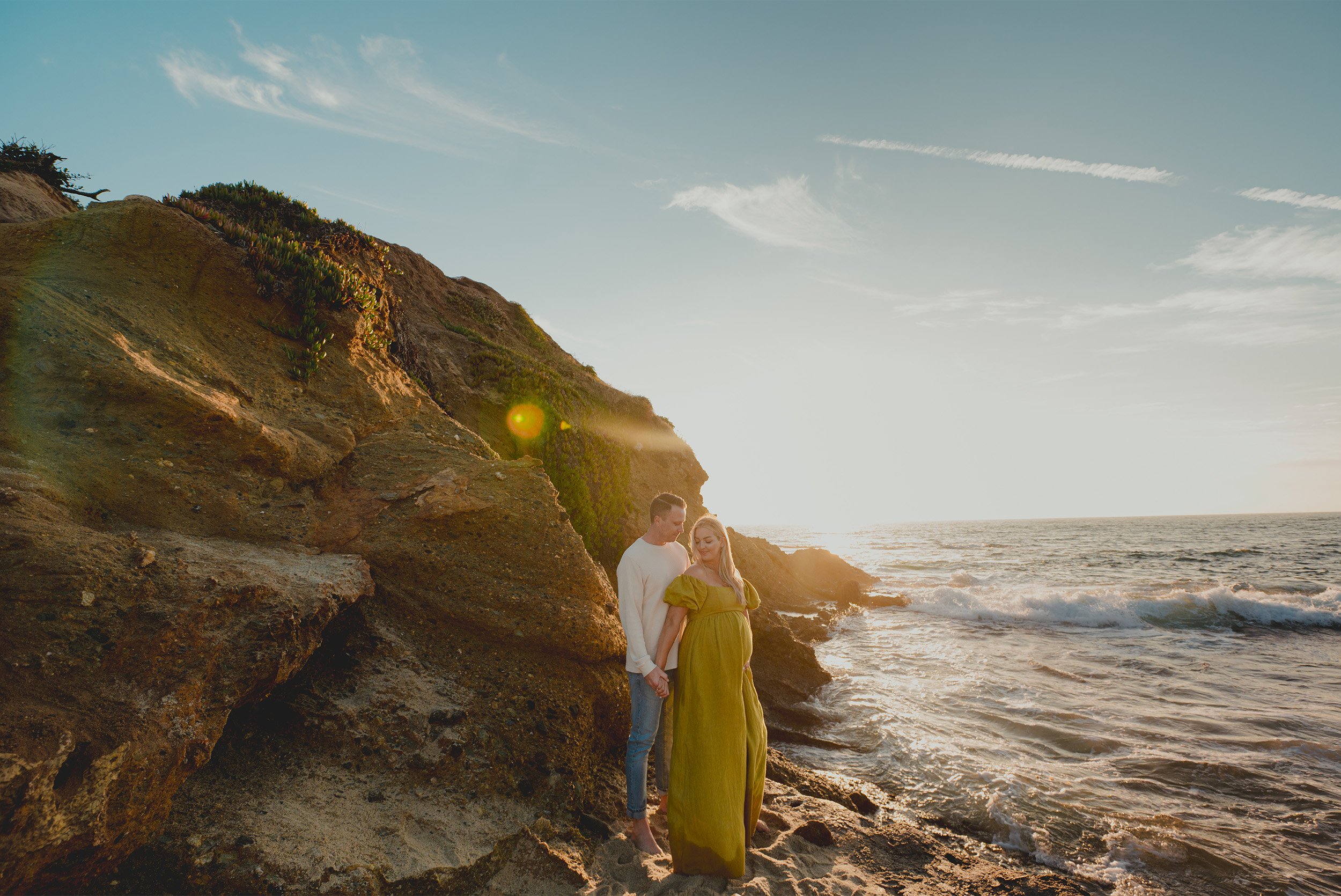 Pregnant couple standing together on cliffside overlooking ocean, highly recommended maternity photographer Orange County