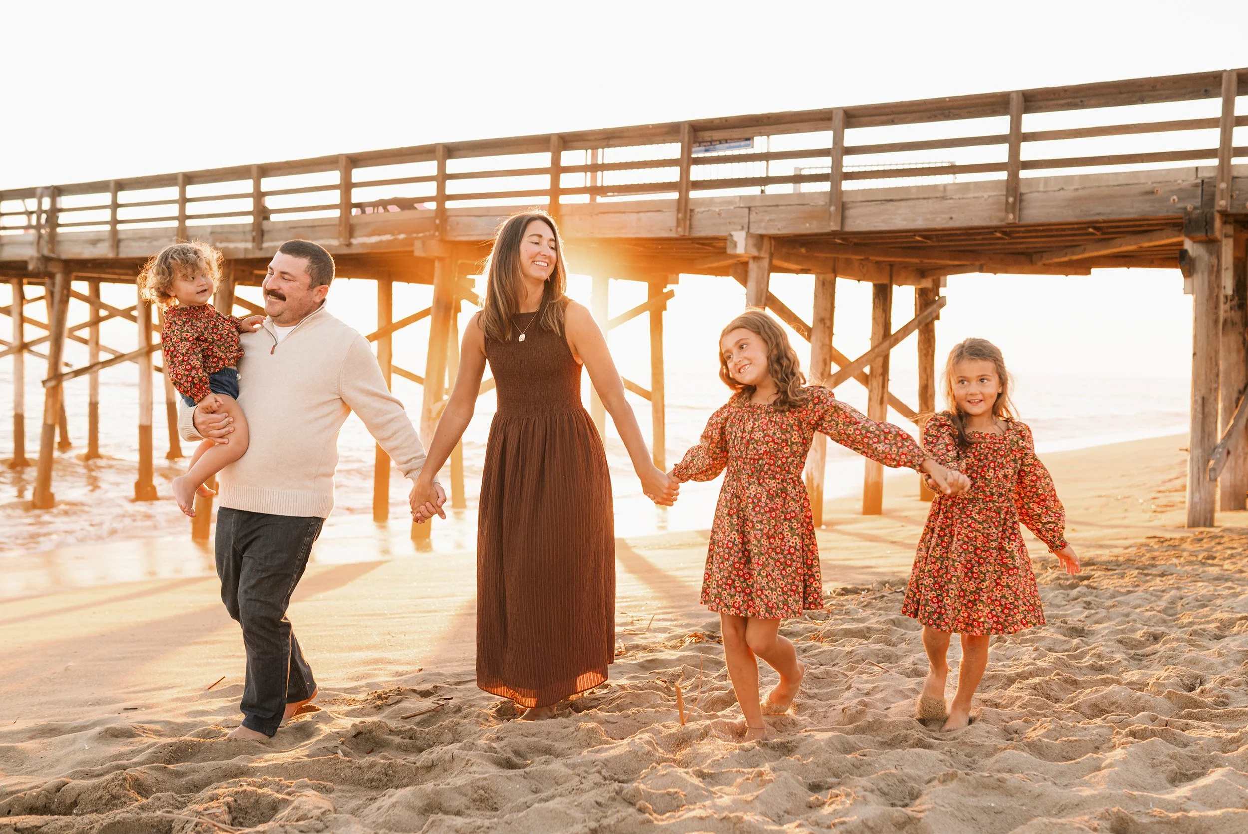 Family beach photography featuring family of five walking together under pier at golden hour, Orange County