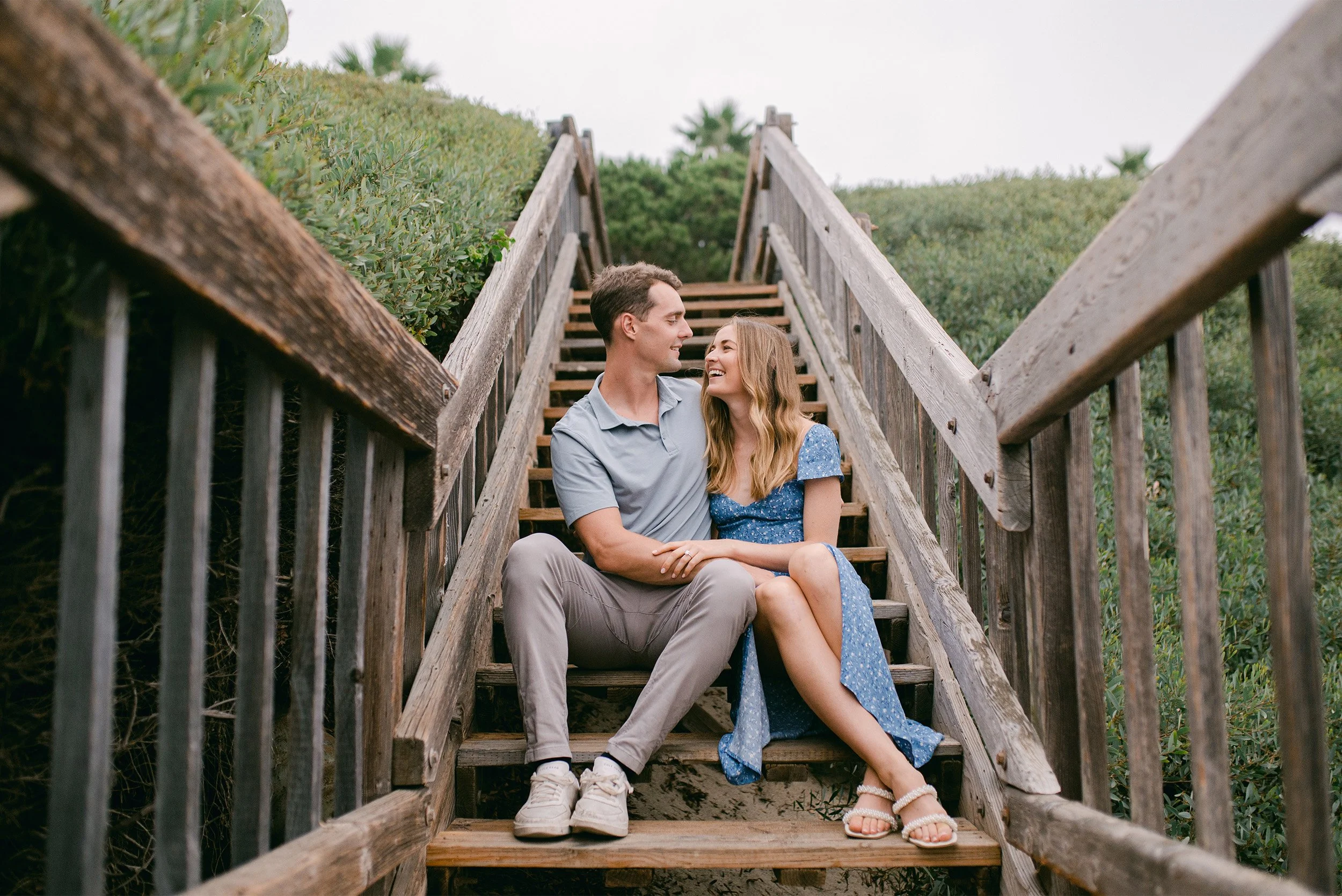 Engaged couple sitting on wooden beach staircase at Crystal Cove, Orange County engagement photographer