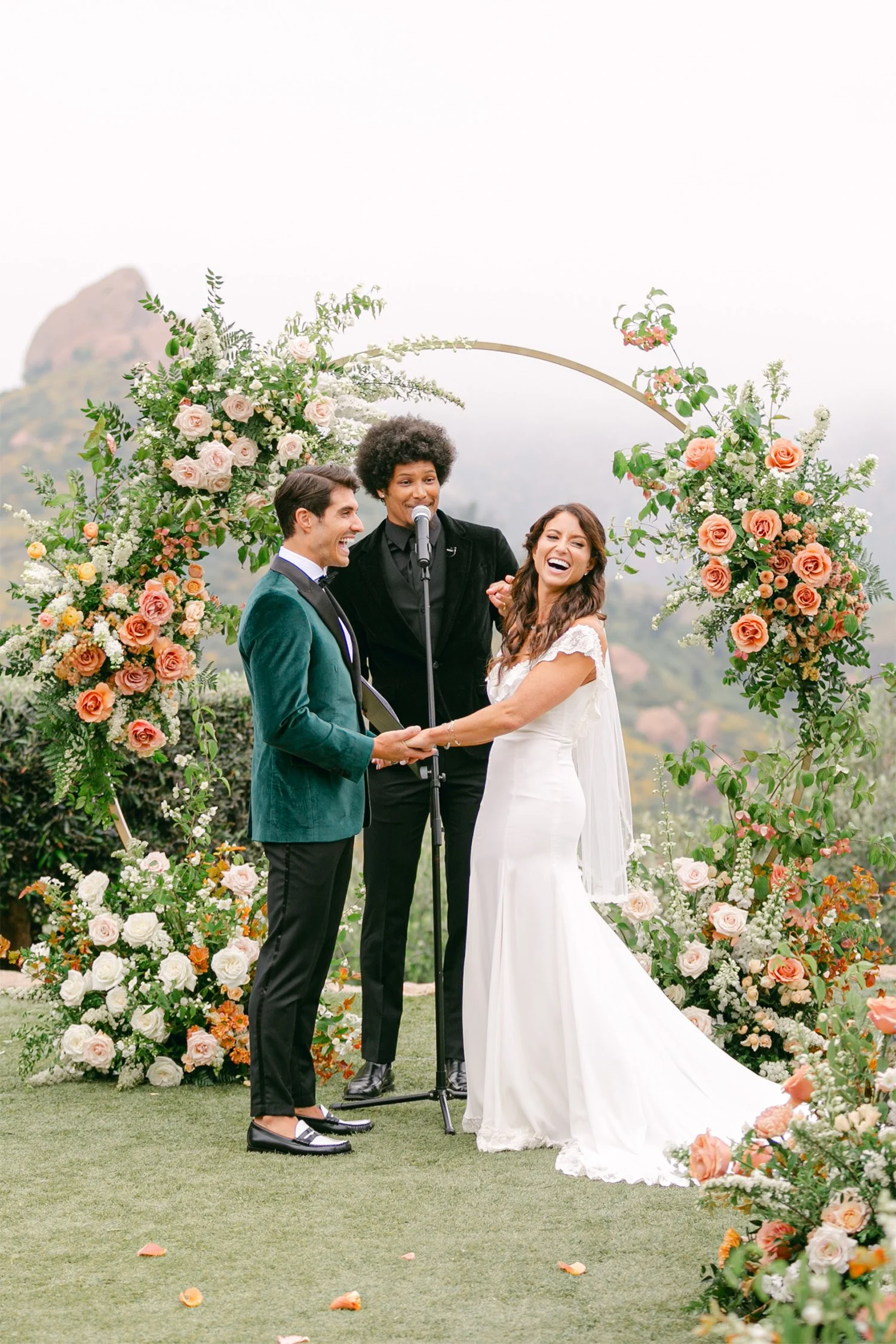 Bride and groom laughing with officiant under floral arch during ceremony, Los Angeles wedding photography at Cielo Farms Malibu