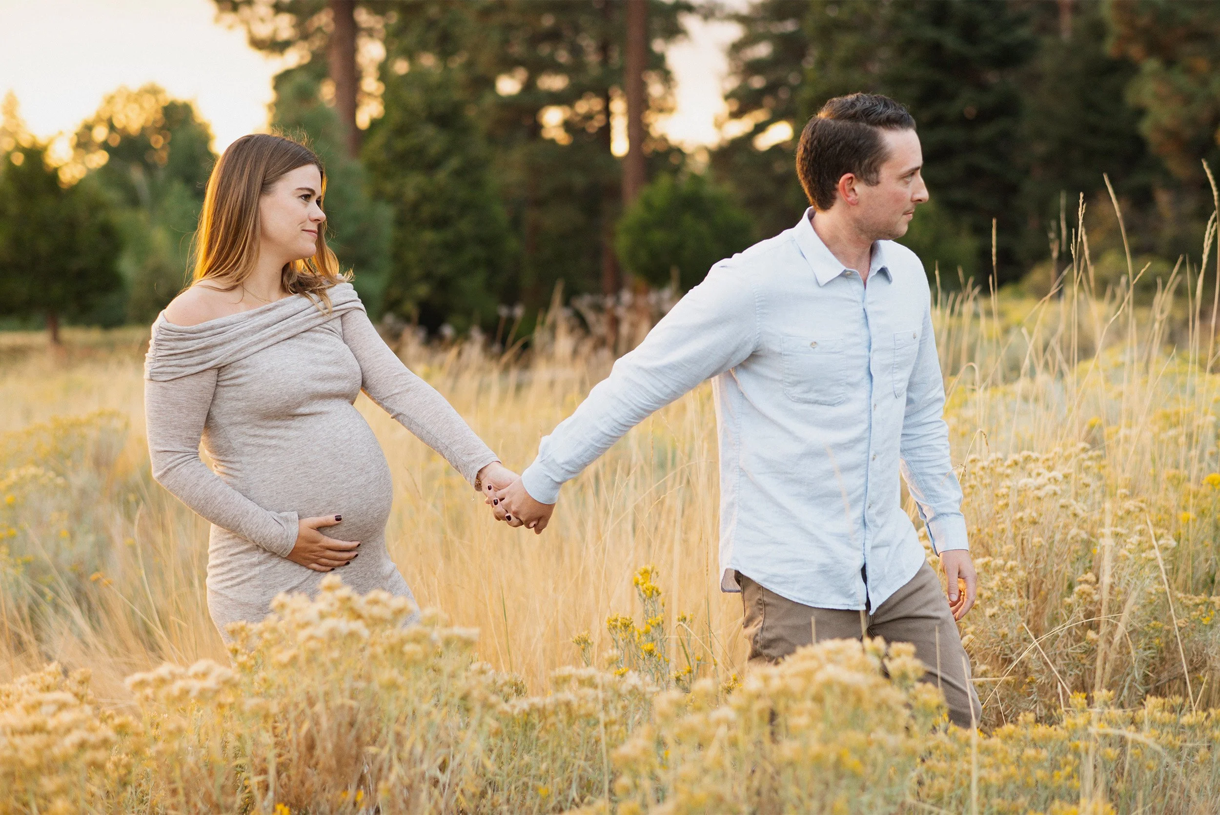 Pregnant couple holding hands walking through golden grass field, Orange County maternity photographer
