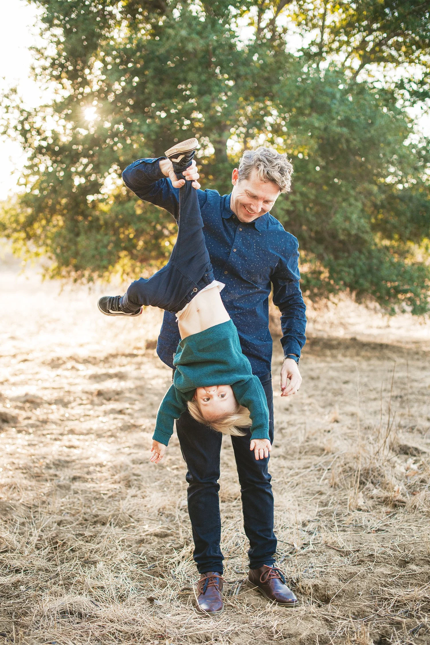 Orange County family photographer captures playful moment of father holding toddler upside down in sunlit field
