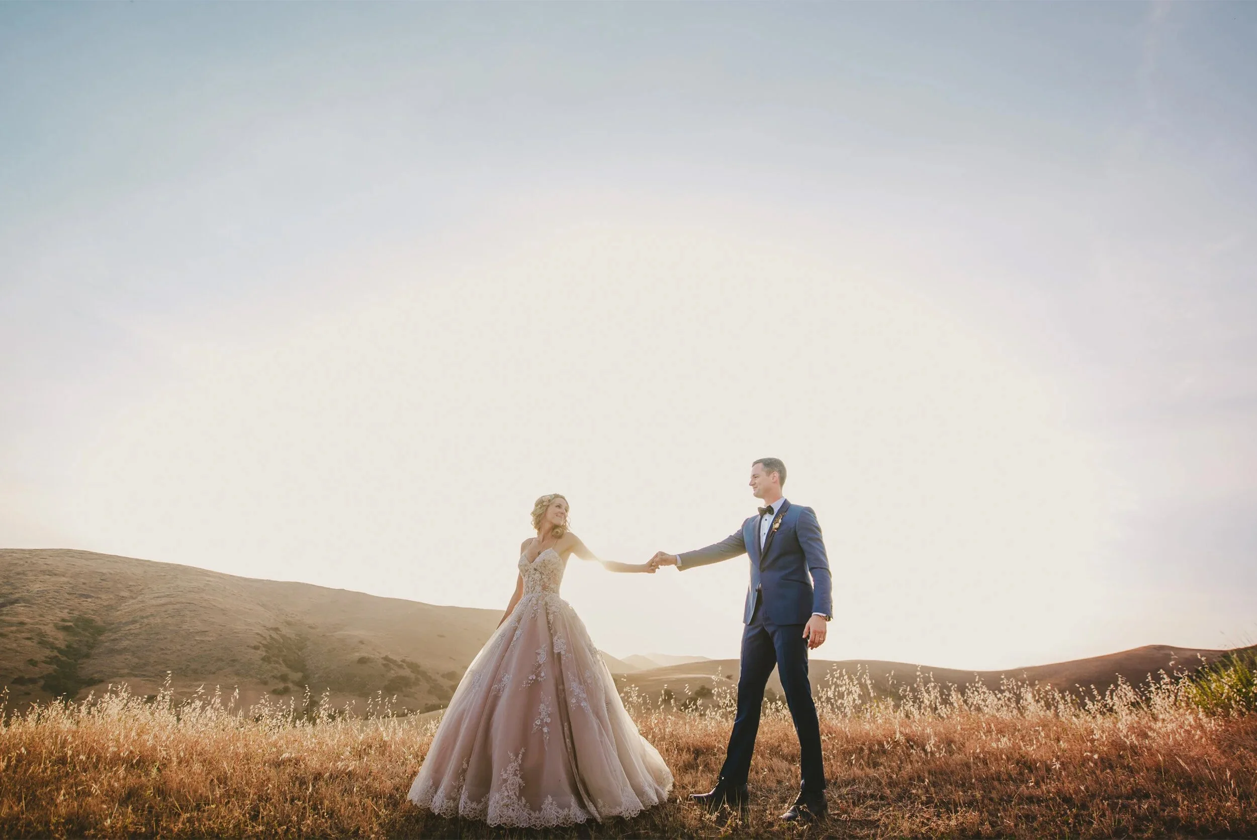 Bride and groom holding hands in a golden field at sunset, Southern California hillside wedding