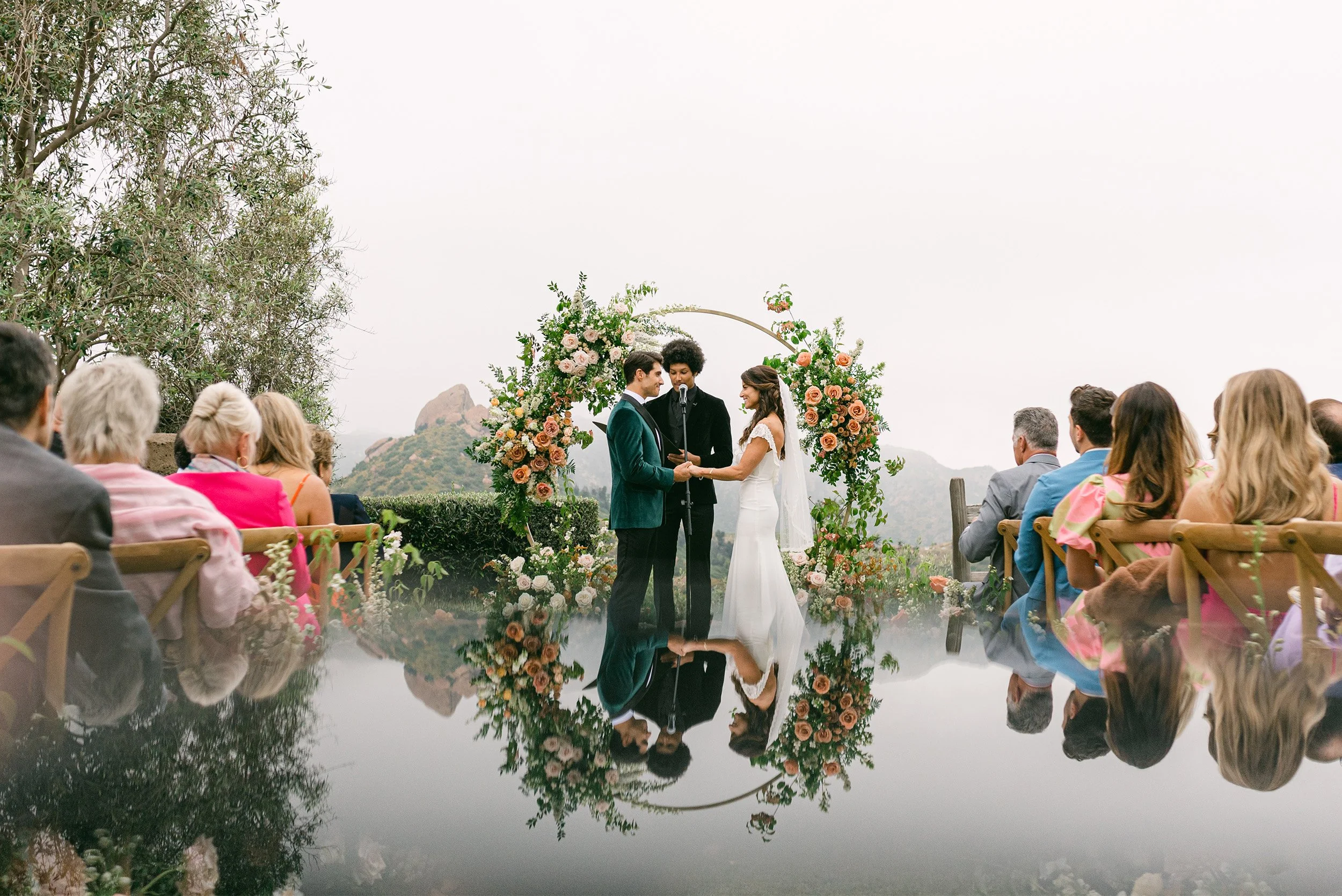 Award-winning wedding photographer in Orange County captures wedding ceremony with stunning mirror reflection pool and floral arch backdrop in Cielo Farms in Malibu wine country