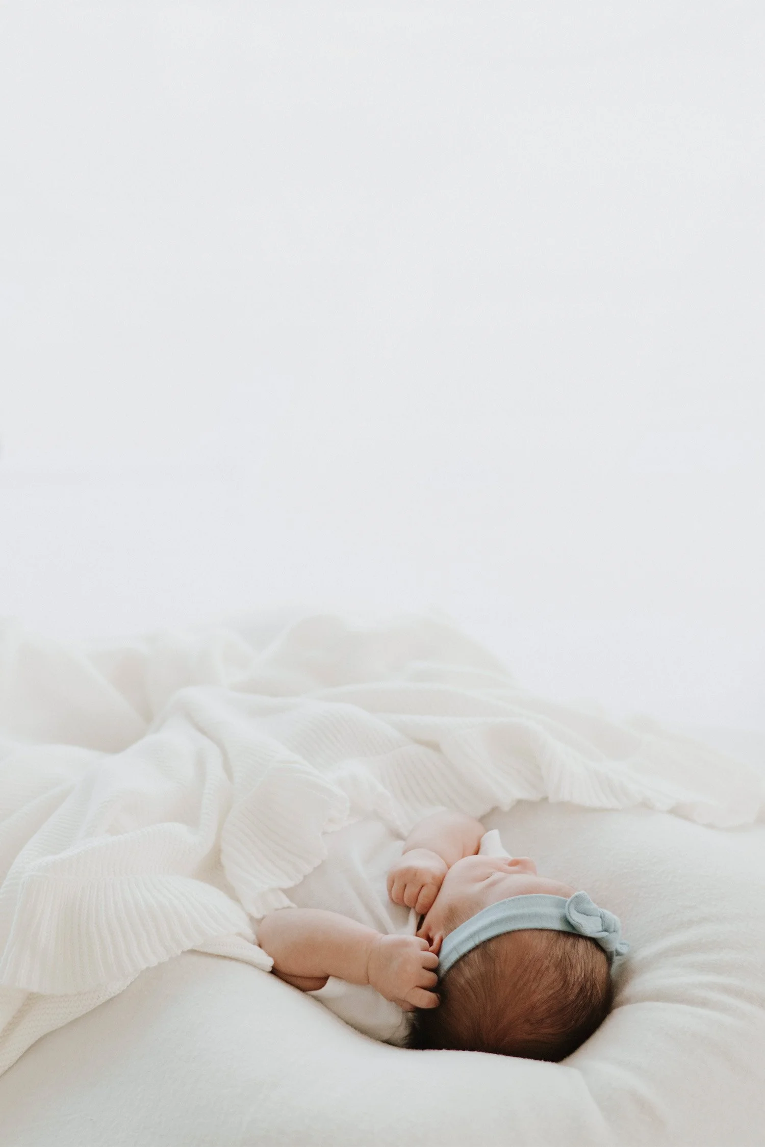 Newborn in blue bow headband lying on white blanket, highly recommended baby photographer Orange County, in home newborn baby photos