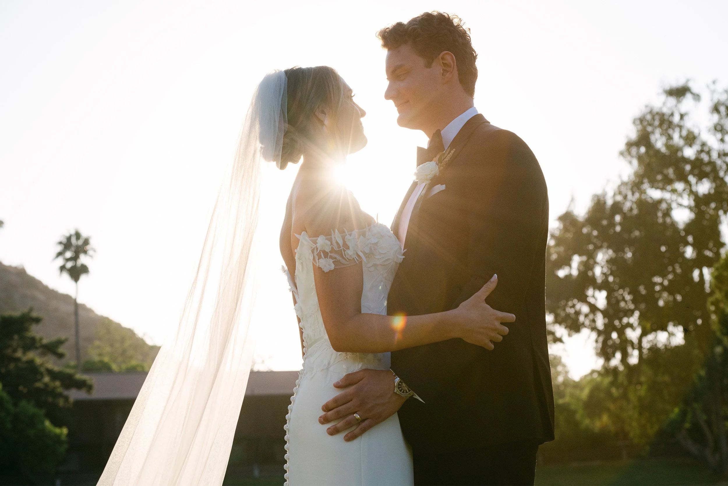 Orange County wedding photographer captures romantic silhouette of bride and groom embracing in golden sunlight with flowing veil at The Ranch at Laguna Beach