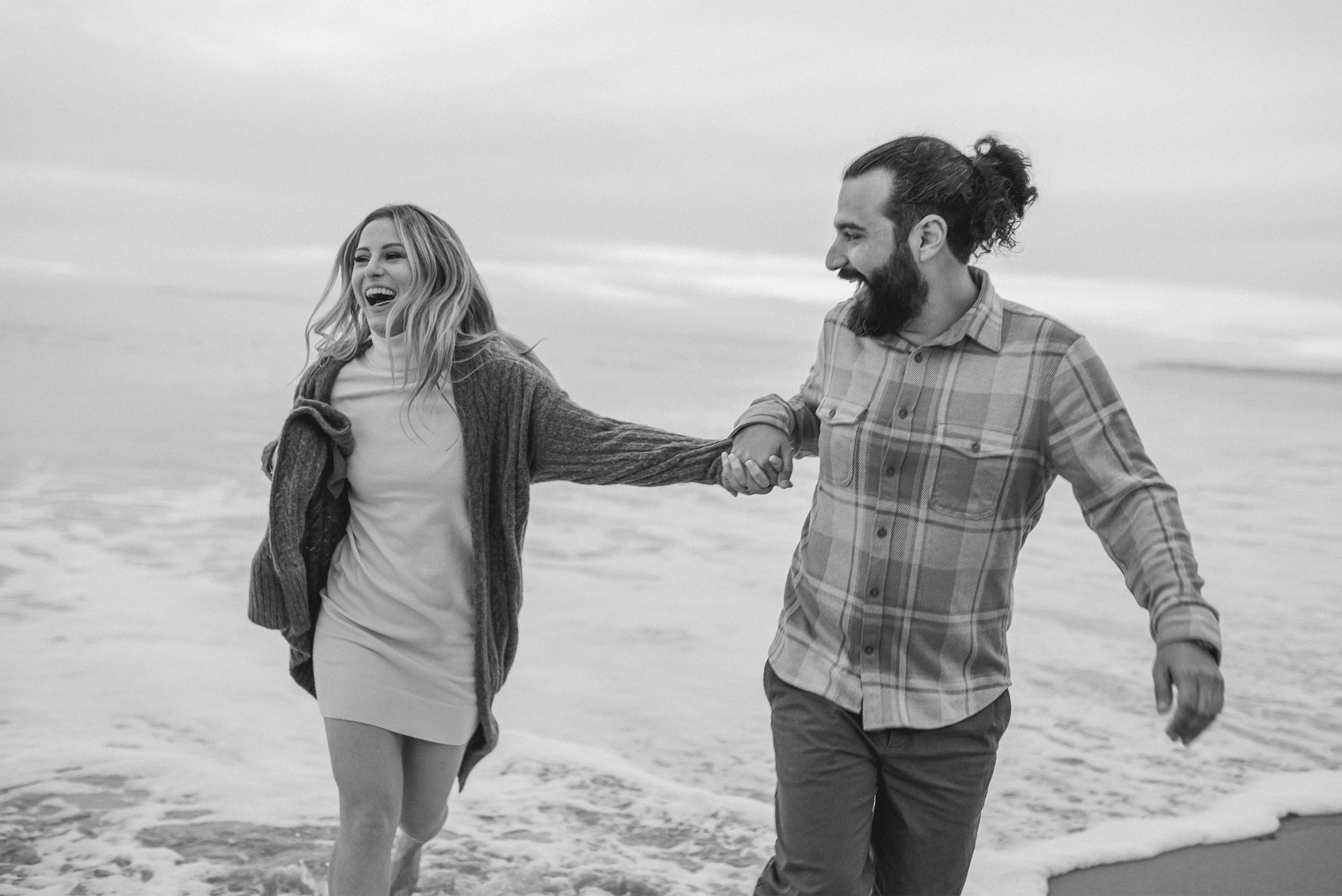 Highly recommended engagement photographer captures couple laughing together while walking along Laguna Beach in black and white