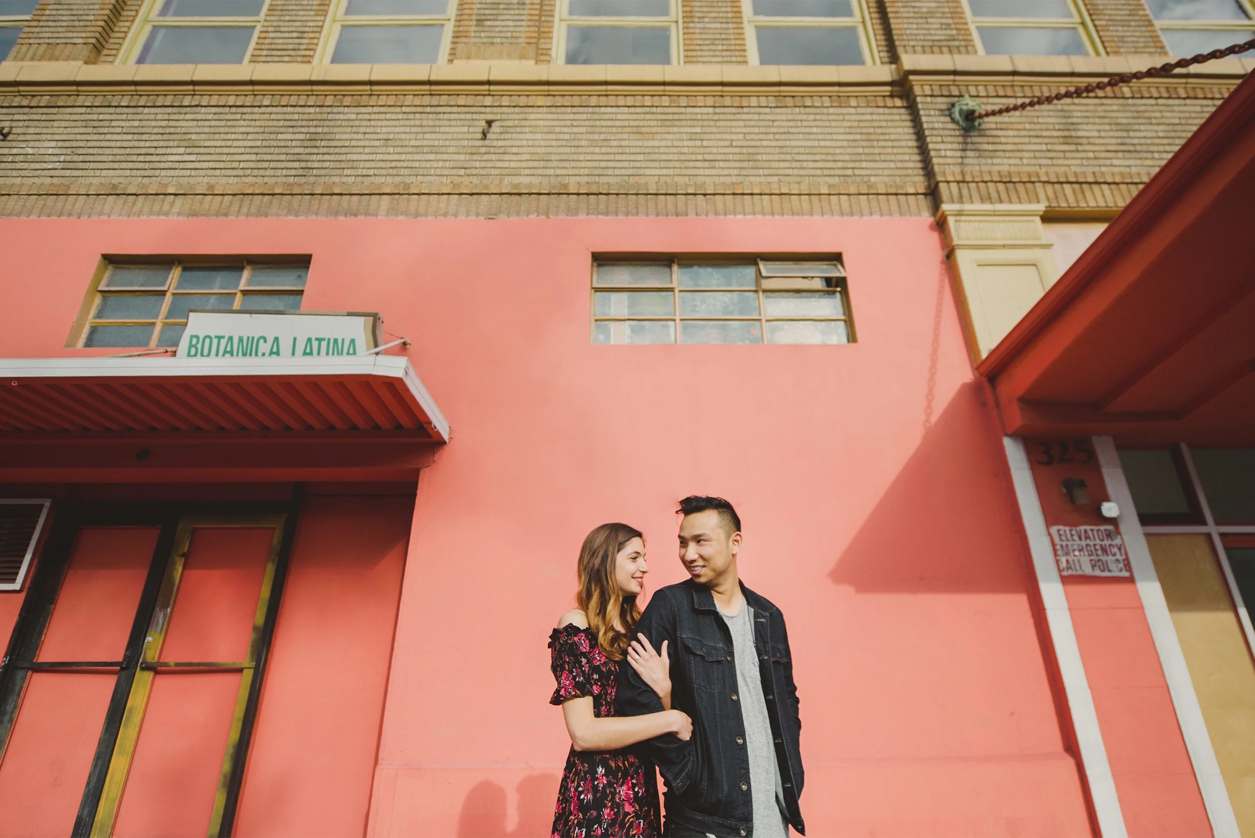 Couple smiling at each other in front of a pink building mural, colorful downtown Los Angeles engagement portrait