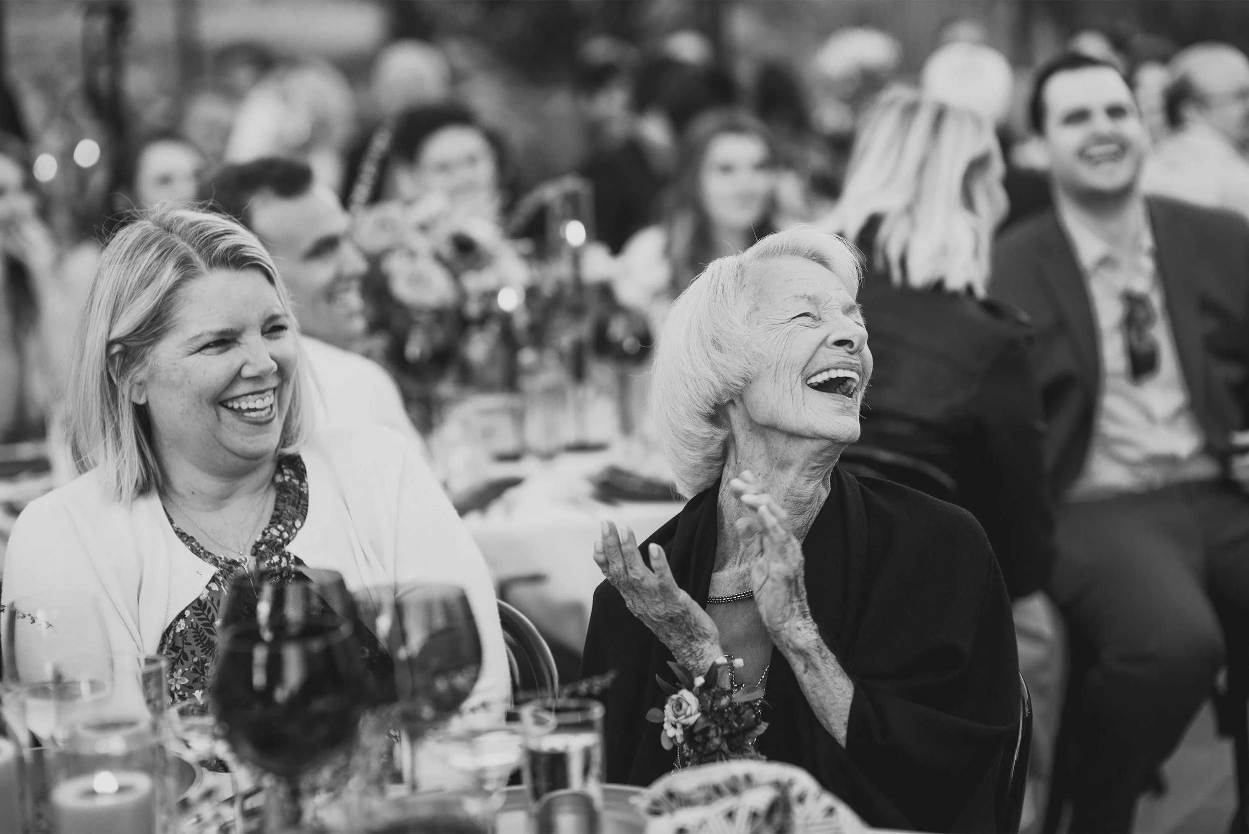 Wedding guests laughing and applauding during reception toast, candid black and white photo