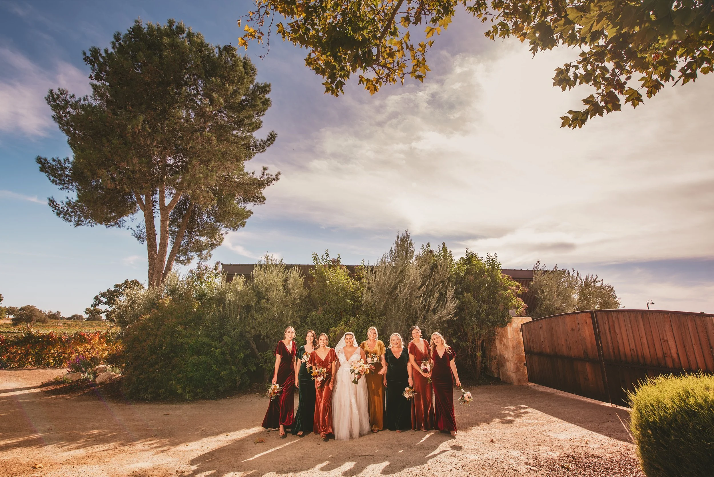 Bride and bridesmaids in jewel-toned velvet dresses walking outdoors at golden hour, Southern California vineyard wedding