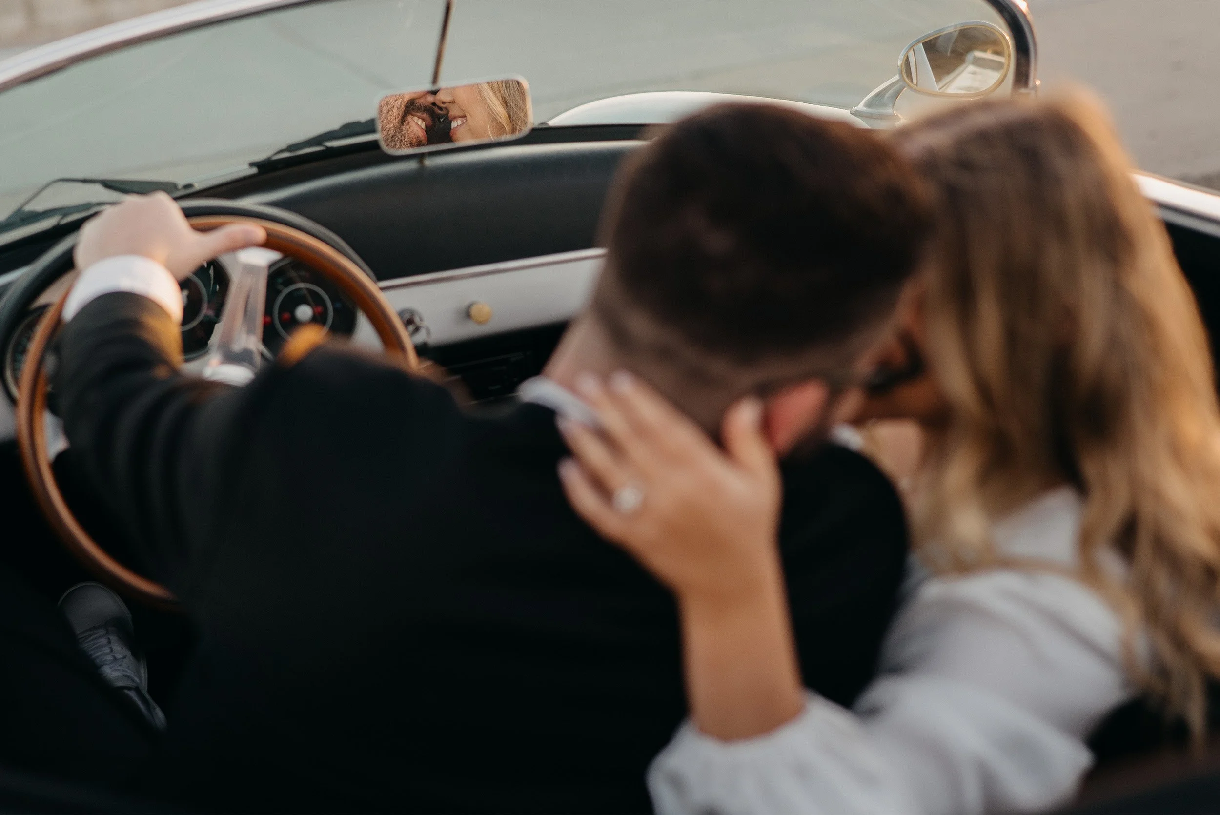 Laguna Beach engagement photographer captures couple kissing in a vintage convertible, framed in the rearview mirror