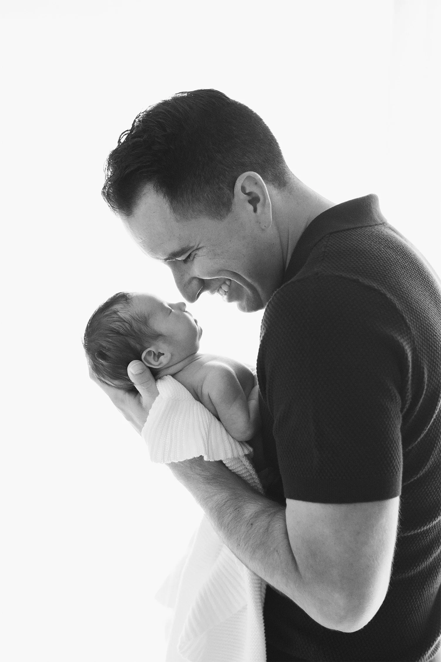 Black and white profile of father smiling at newborn in his arms, award-winning baby photographer in Orange County