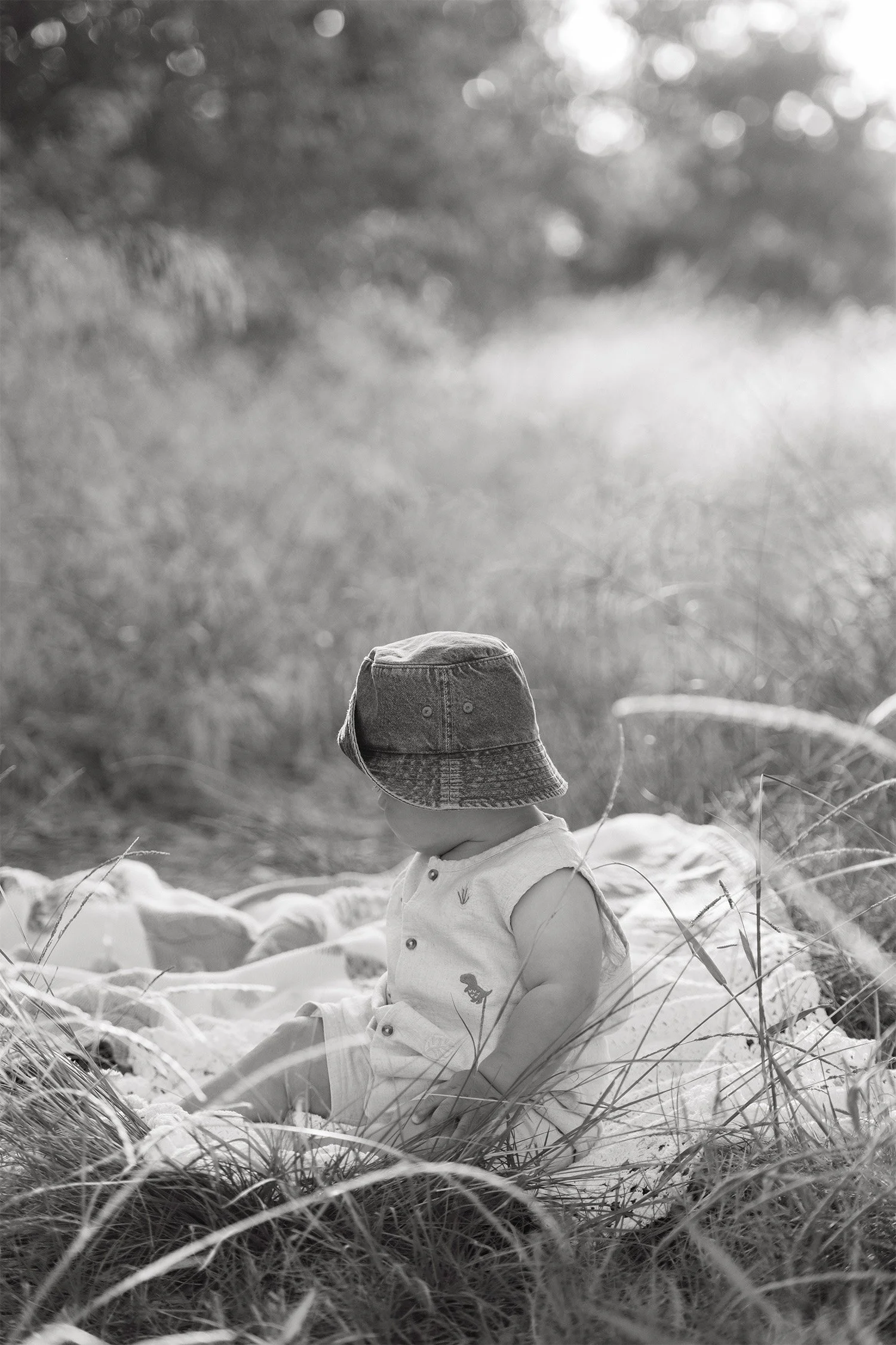 Family photography session featuring toddler in a bucket hat sitting in tall grass, black and white close up image