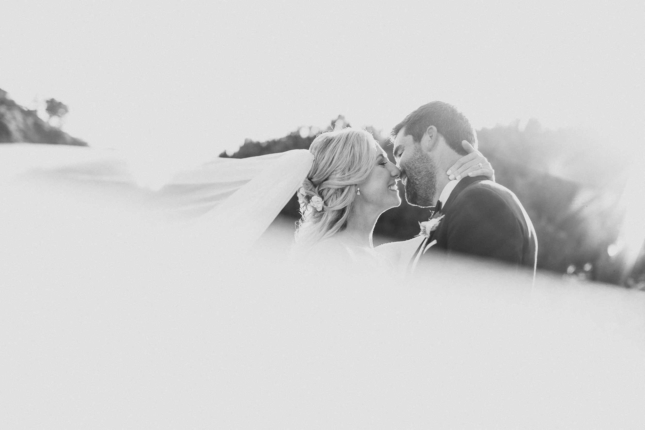 Bride and groom noses touching in windswept veil, black and white Orange County wedding photography at The Ranch at Laguna Beach
