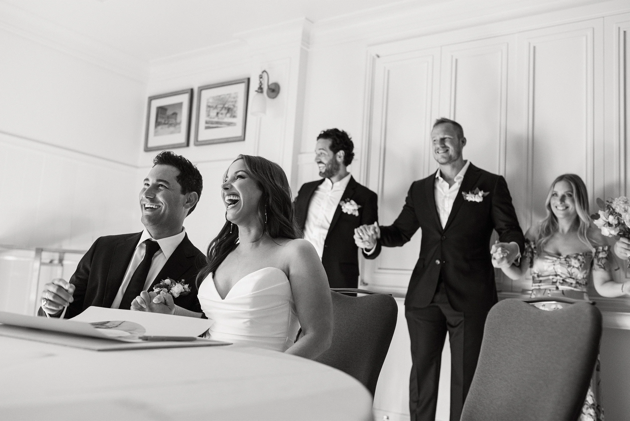 Orange County wedding photographer captures joyful moment surrounded by laughing wedding party at a, black and white