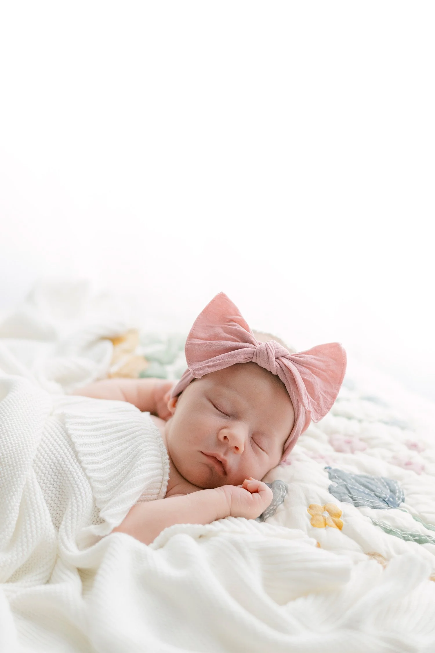 Sleeping newborn in pink bow headband on floral quilt, highly recommended newborn photographer located in Orange County
