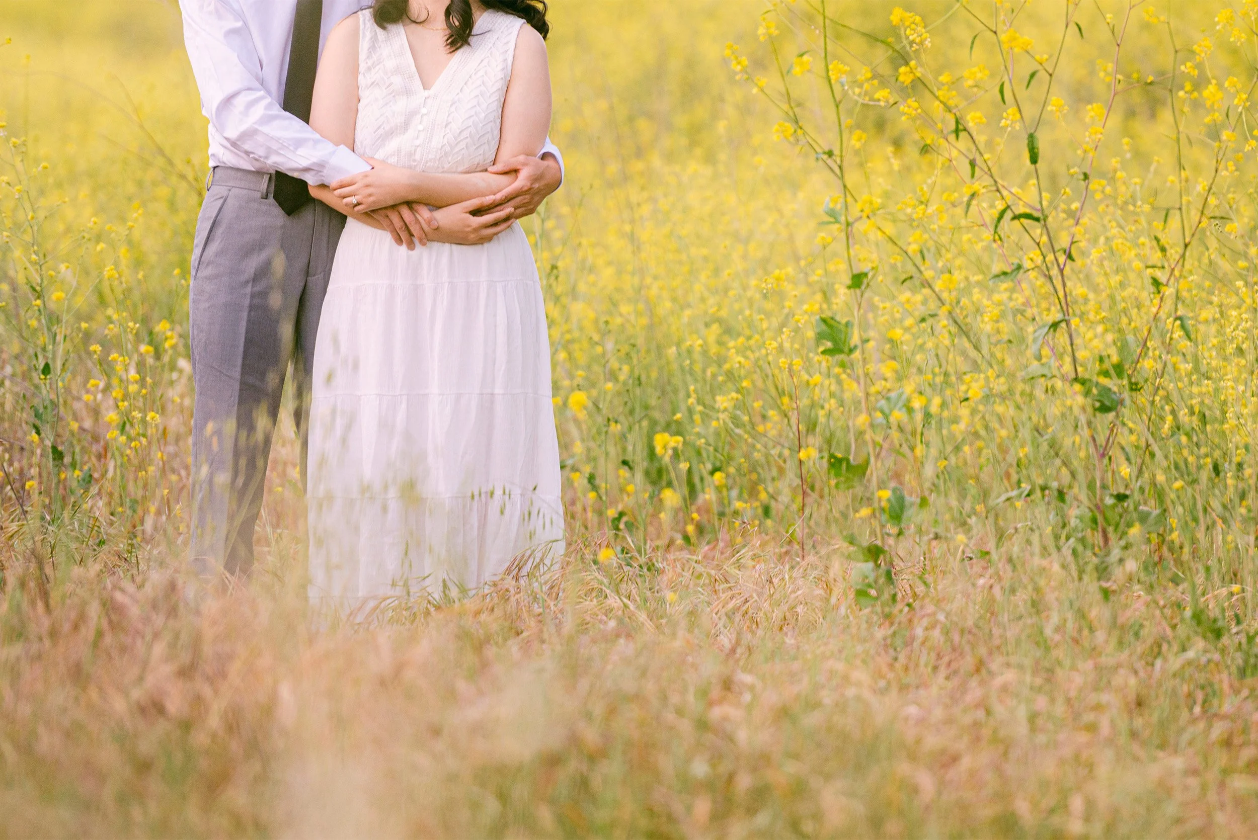Close-up of couple holding hands in yellow wildflower field, highly recommended engagement photographer in Orange County