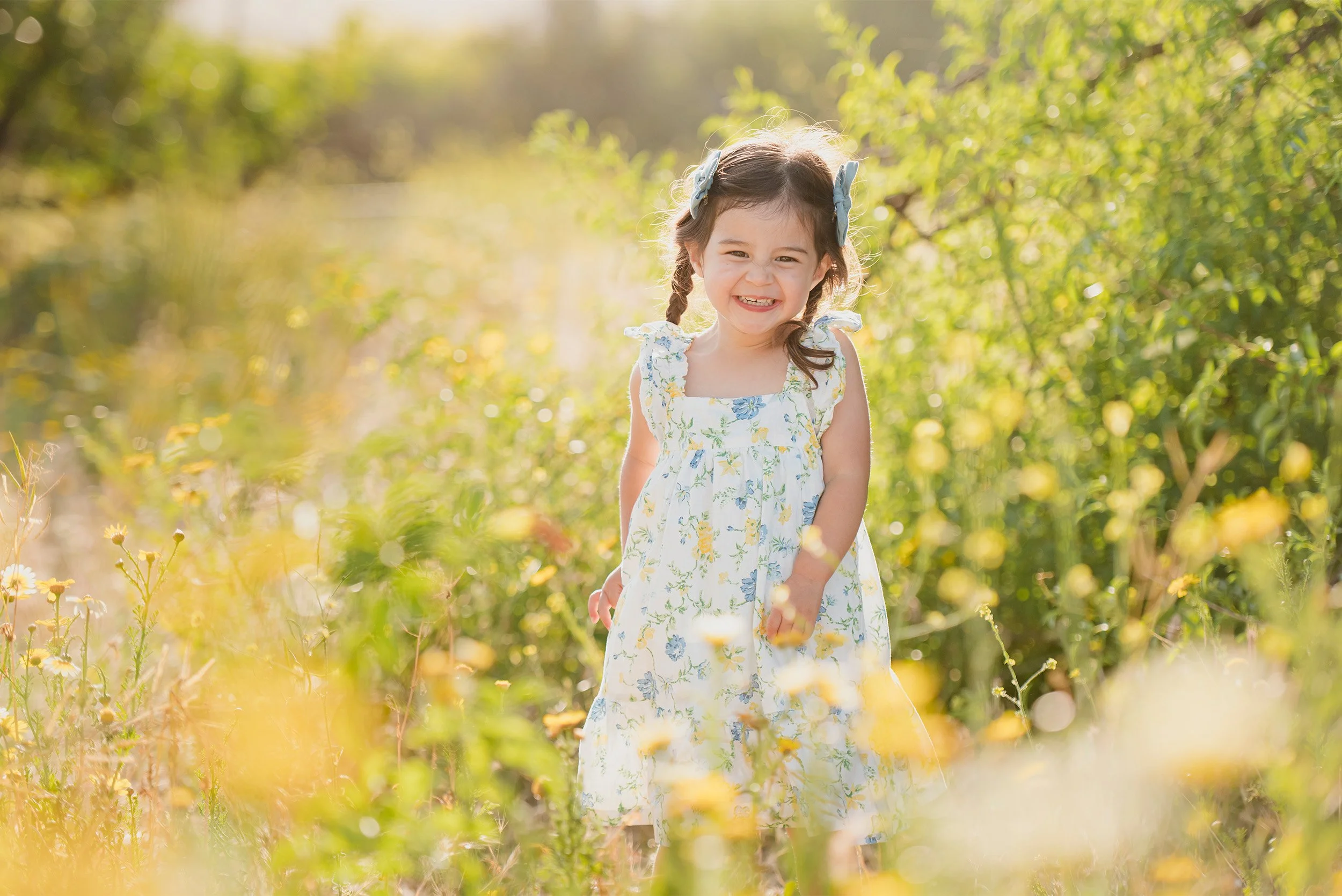 Young girl in floral dress smiling among yellow wildflowers, Family photography session in Orange County