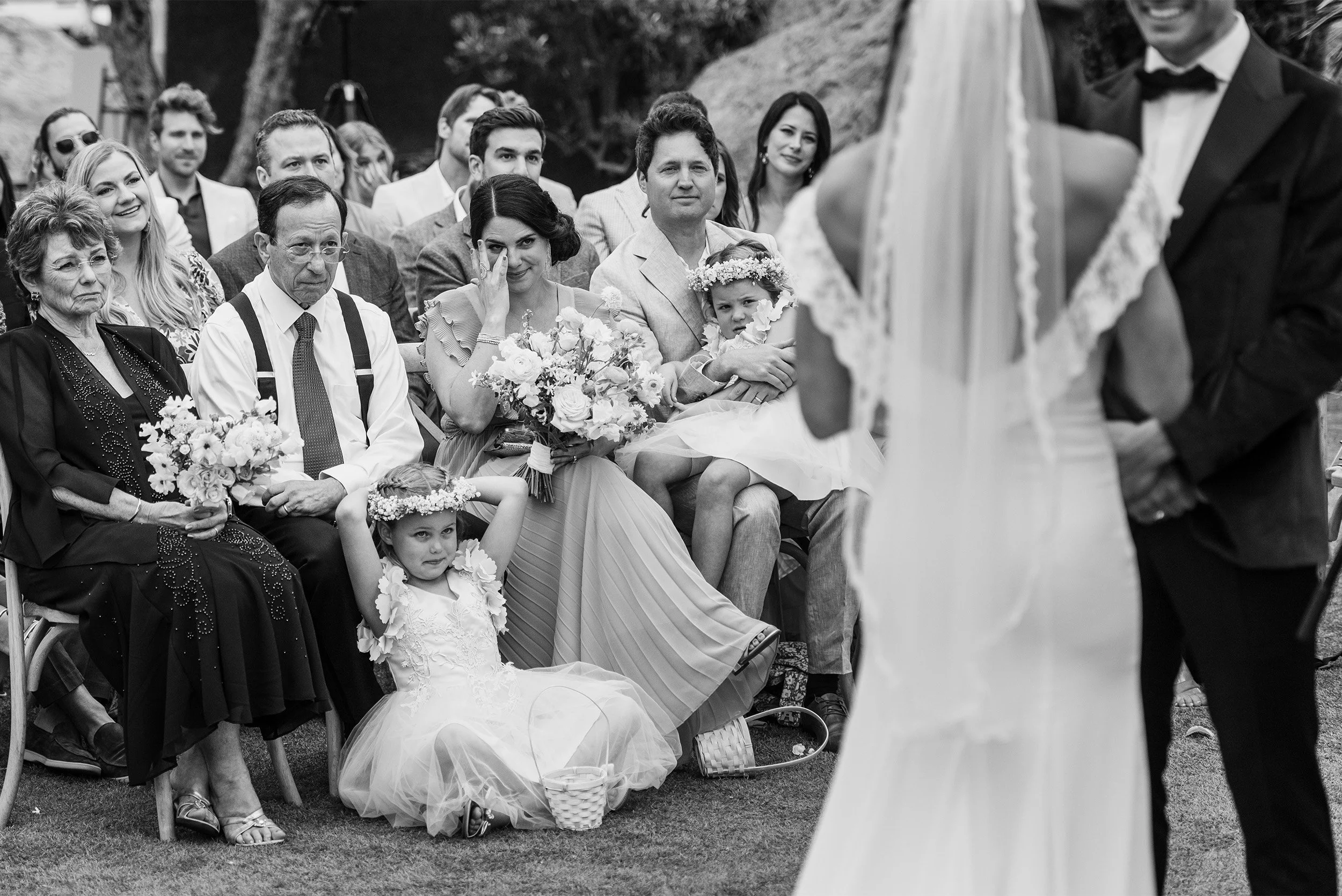 Wedding guests seated in chairs watching bride and groom during outdoor ceremony at Cielo Farms Malibu, black and white candid photo