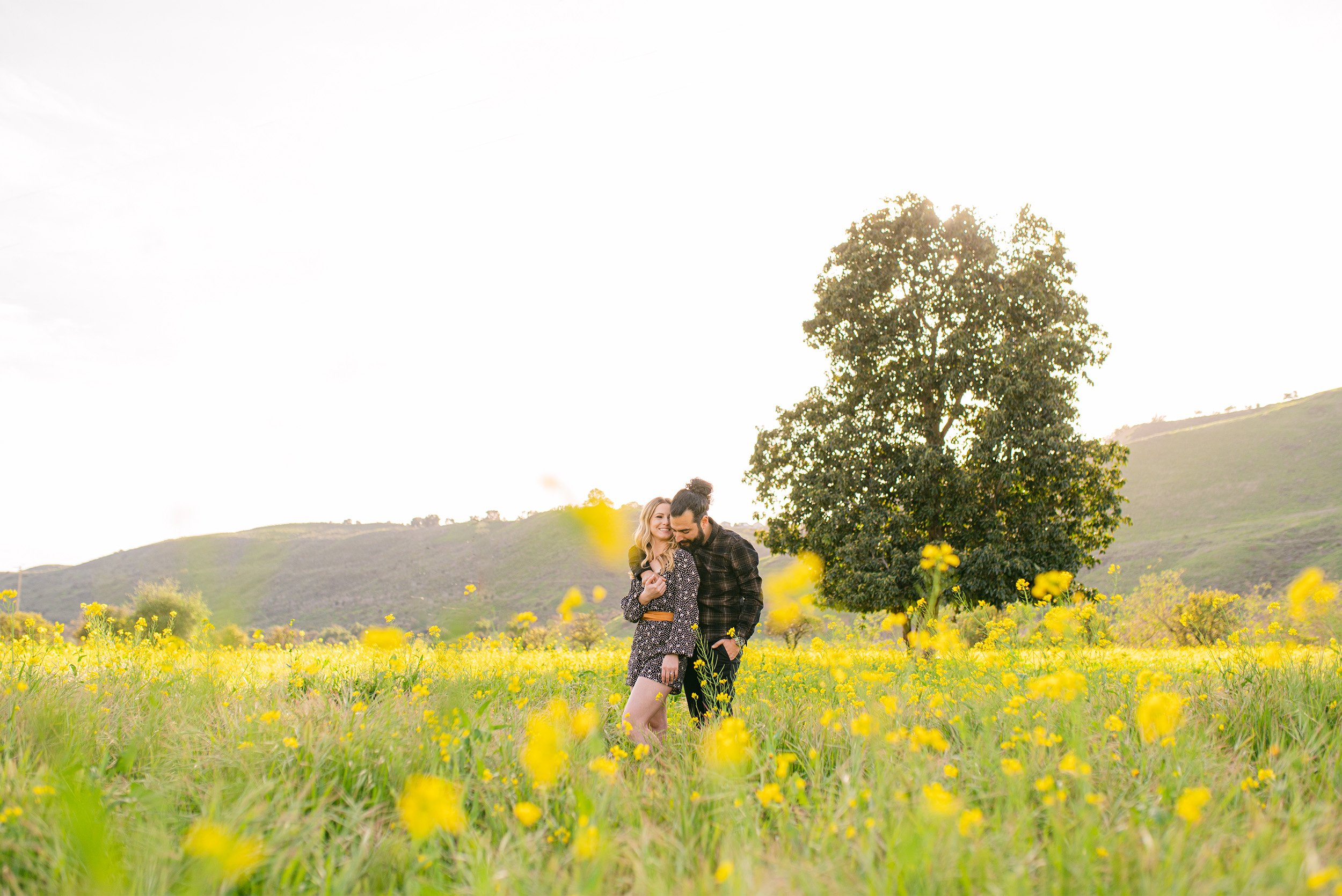 Award-winning engagement photographer in Orange County captures couple embracing in a blooming yellow wildflower field