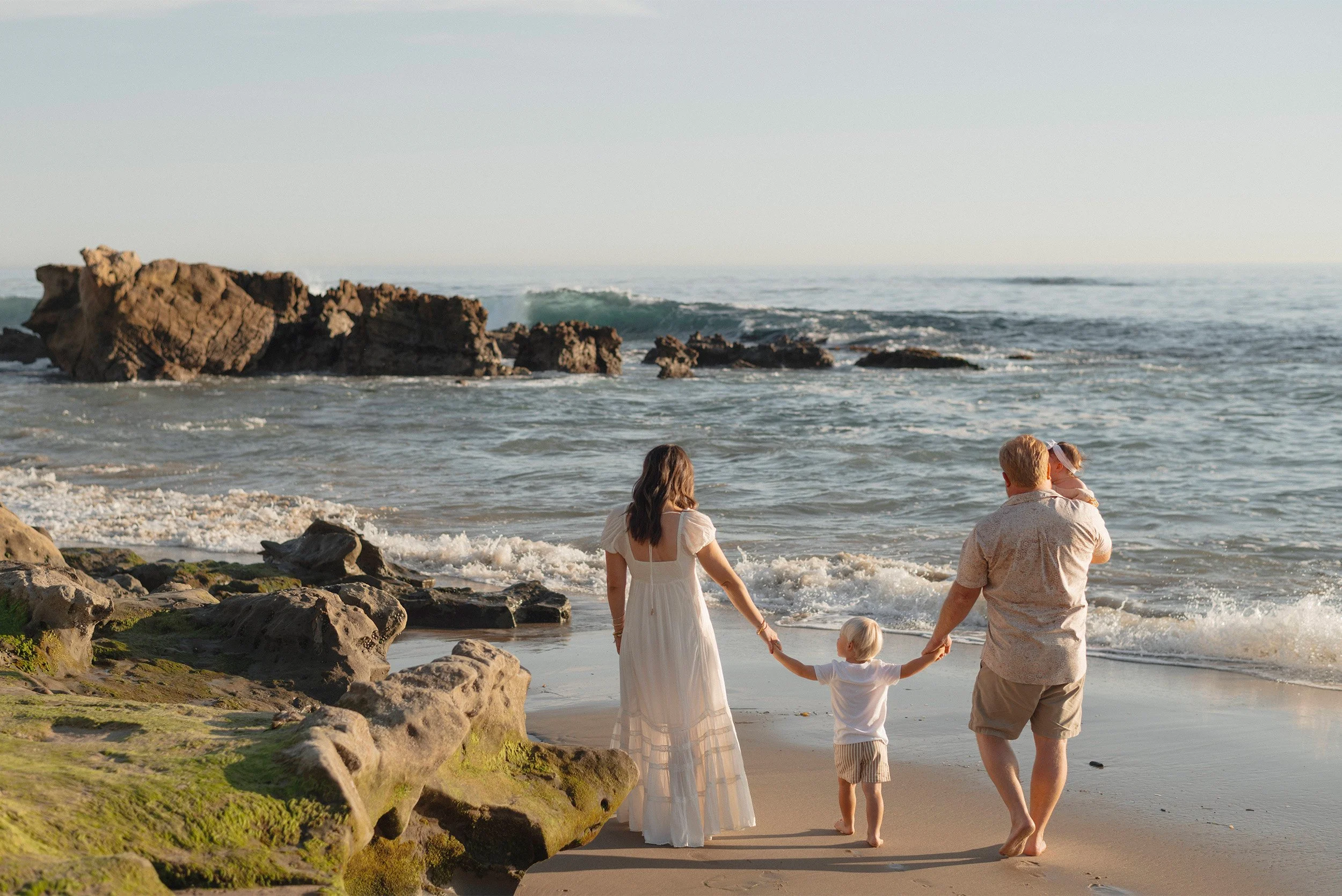 Orange County family photographer captures family walking along rocky coastline in Laguna Beach at golden hour