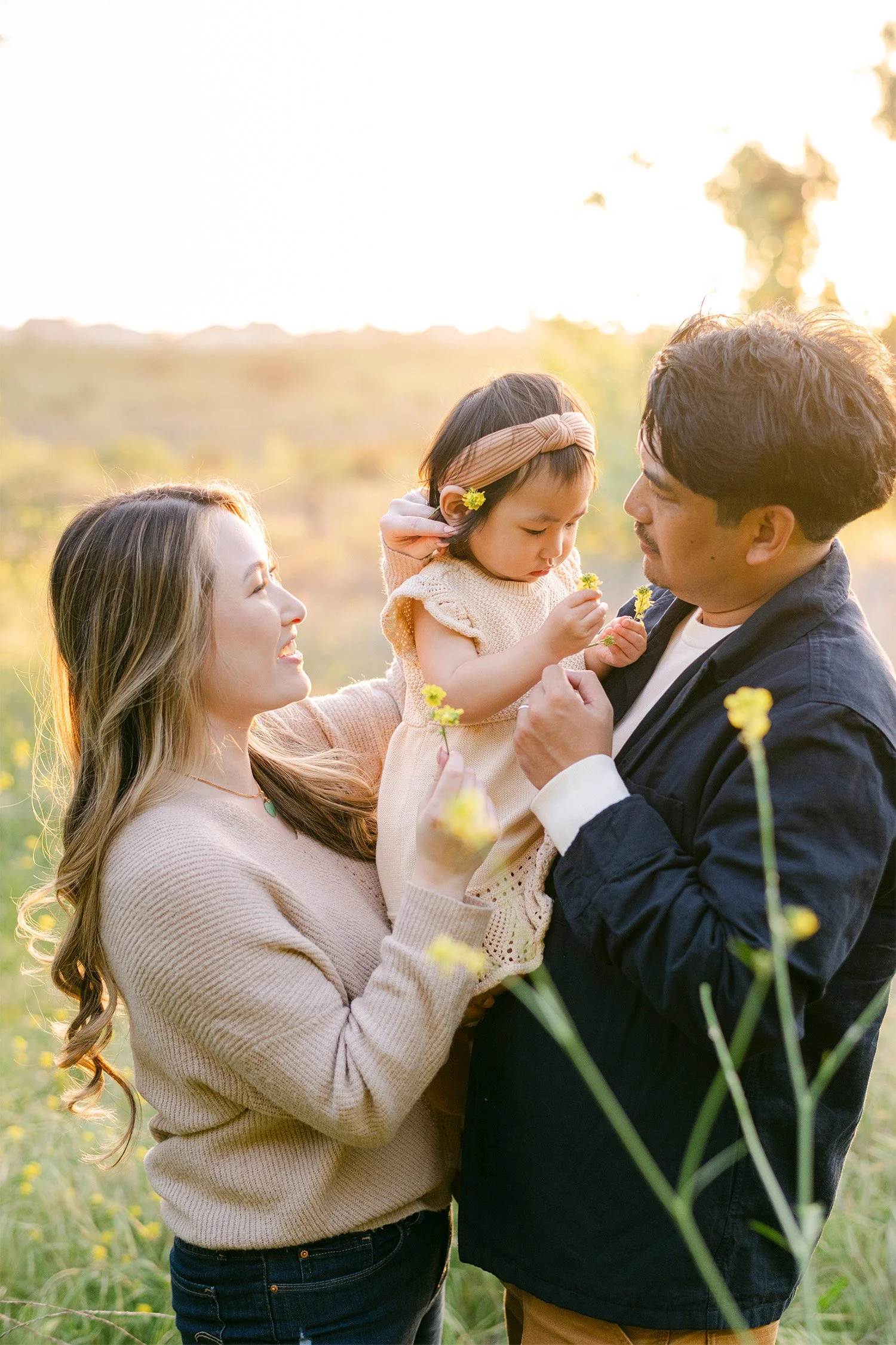 Award-winning family photographer in Orange County captures parents admiring their daughter as she holds a wildflower
