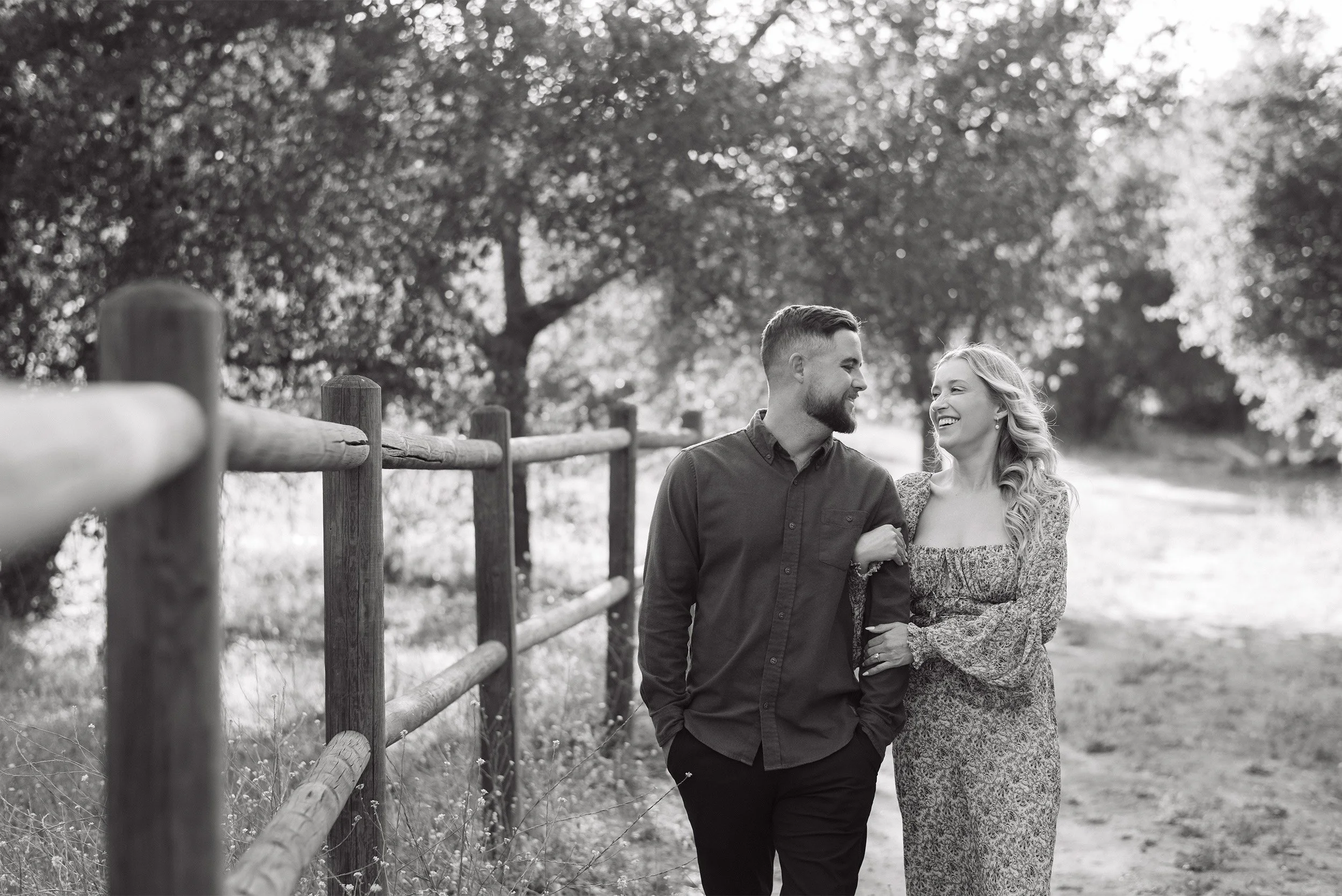 Orange County engagement photographer captures candid black and white moment of couple laughing beside a wooden fence