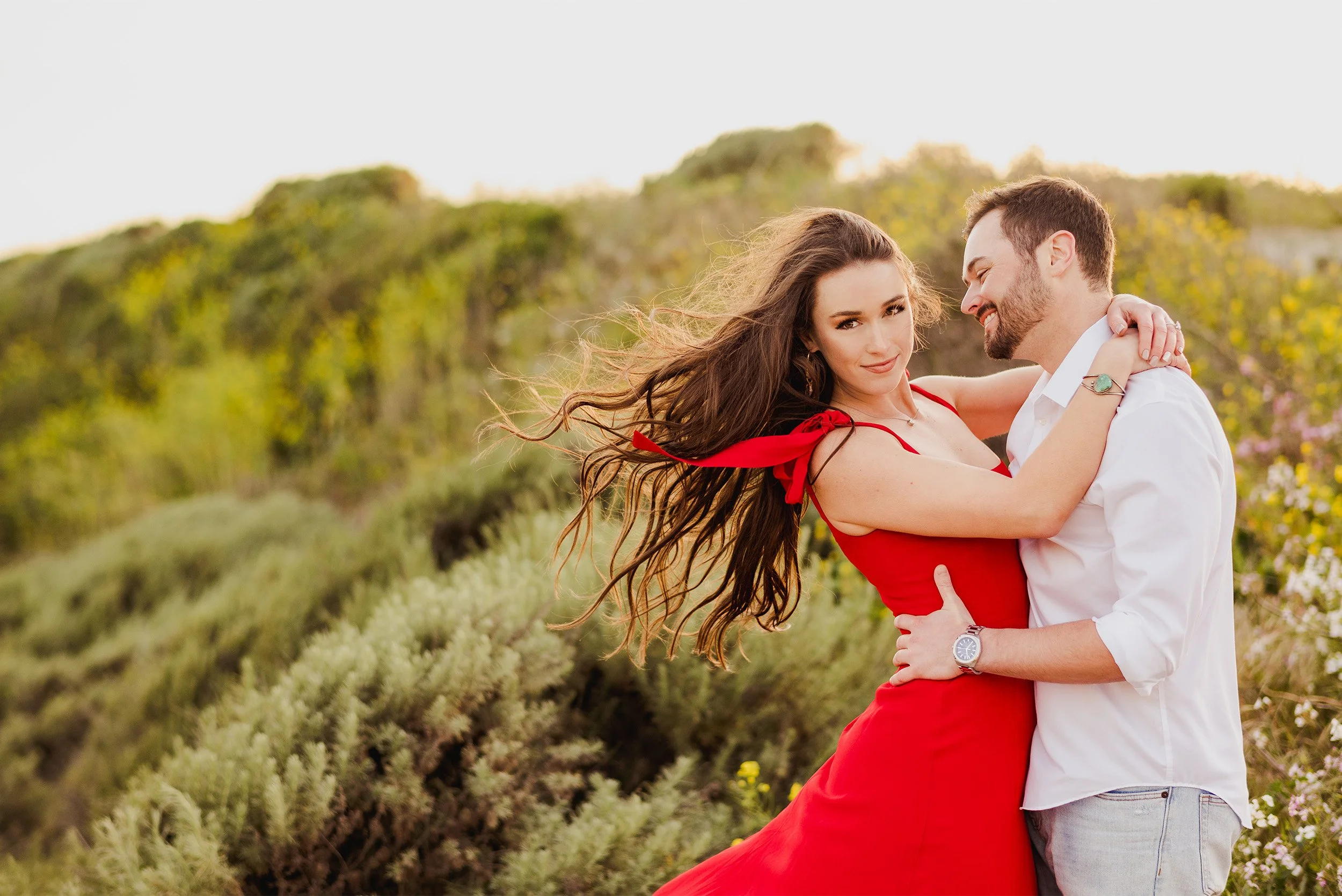 Bride-to-be in red dress twirling with fiancé in golden field, highly recommended engagement photographer in Orange County